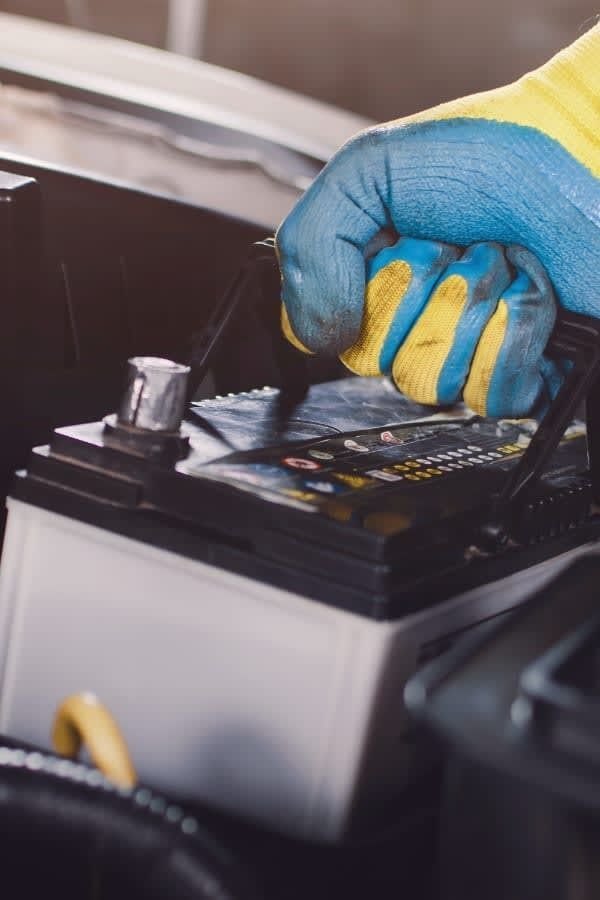 Hand in a blue and yellow glove removing a car battery.