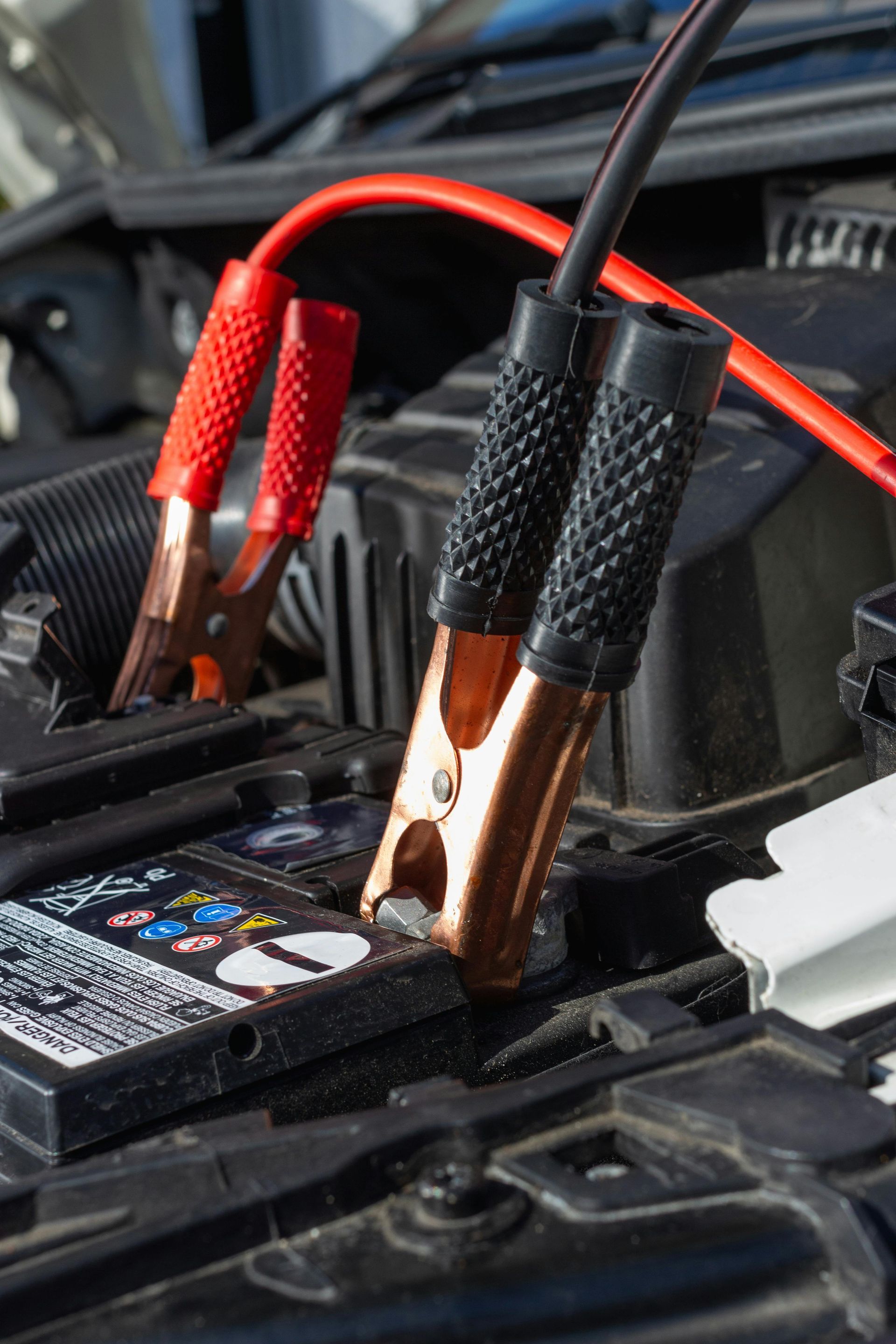 Hands in gloves connecting jumper cables to a car battery.