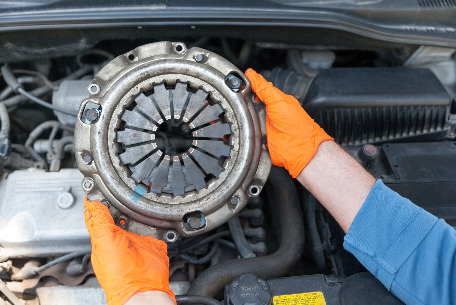 A person is holding a clutch plate in their hands in front of a car engine.