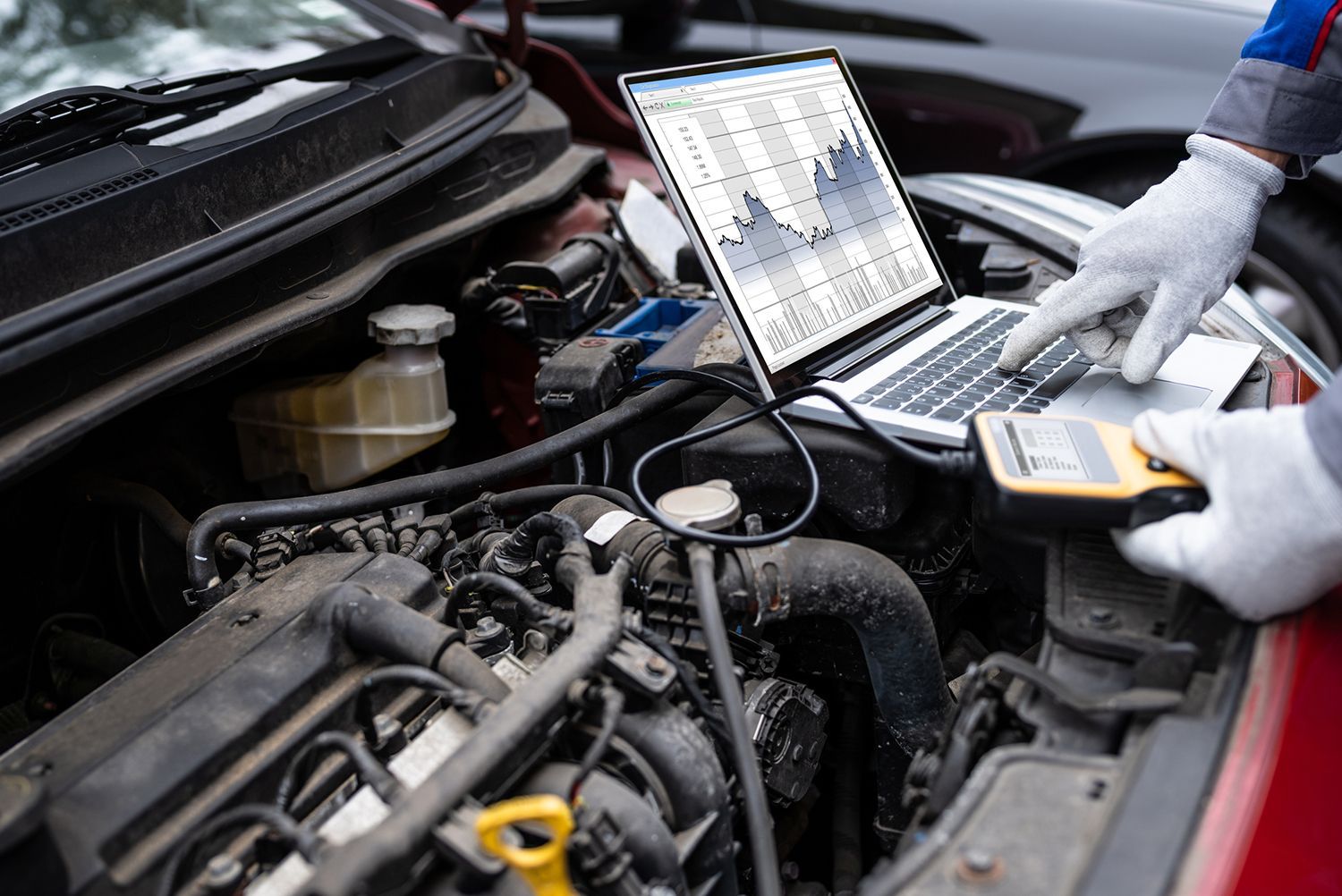 A person is working on a car engine with a laptop.