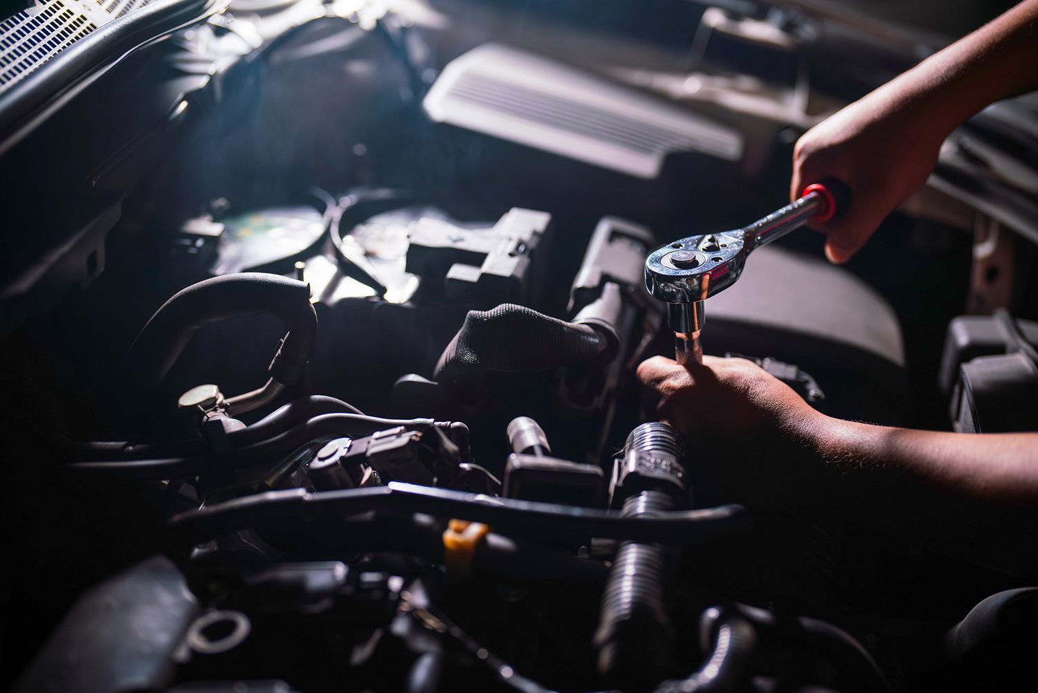 A person is working on the engine of a car with a wrench.
