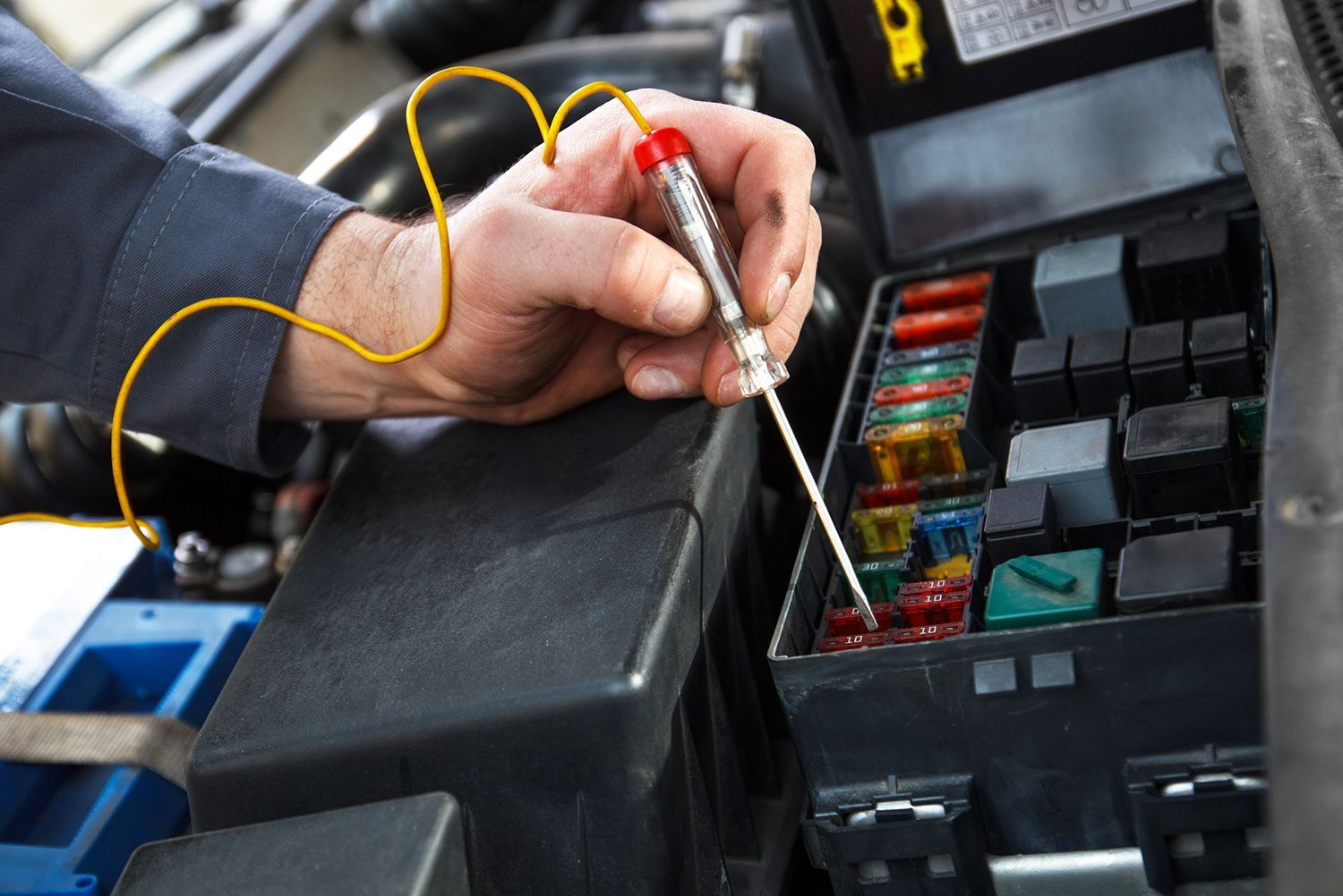 A man is working on a car with a voltage tester
