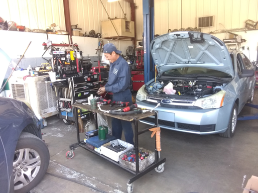 A man is working on a car in a garage with the hood open.