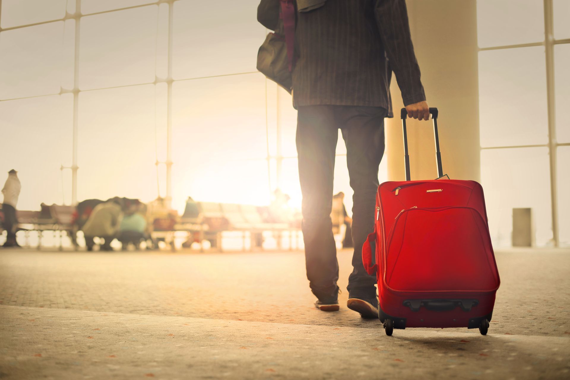 Man walking towards and airport with a red suitcase