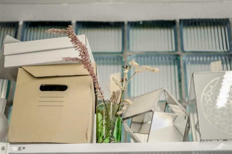 A shelf with boxes and a vase of flowers on it.