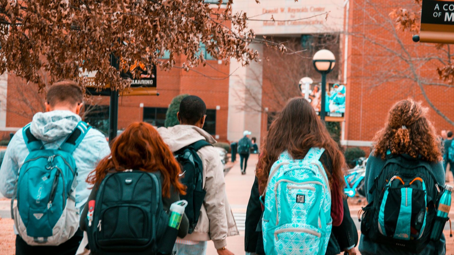 A group of students with backpacks are walking down a sidewalk.