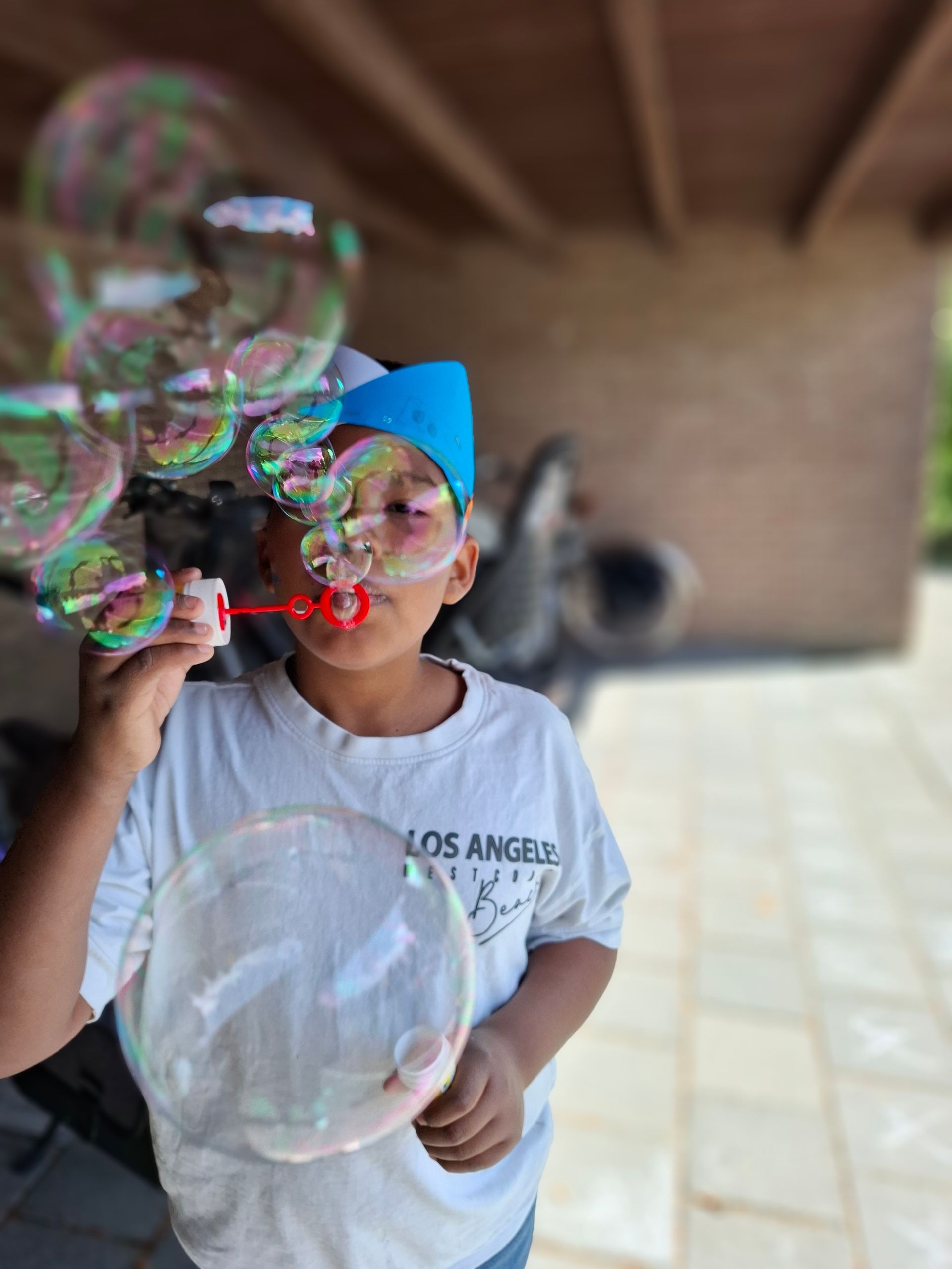 A boy blowing soap bubbles wearing a los angeles shirt
