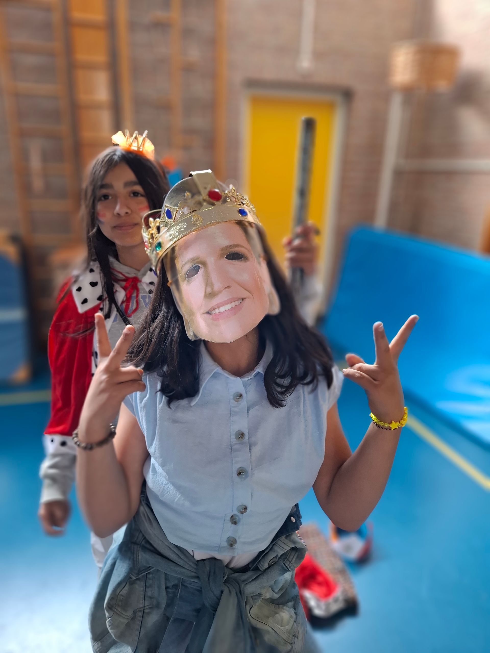 A girl wearing a mask and a crown is standing next to another girl