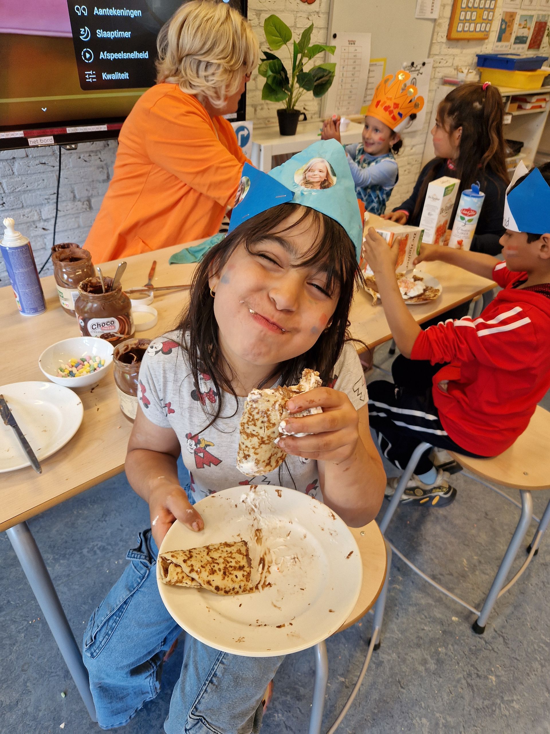 A little girl is holding a plate of food in a classroom.