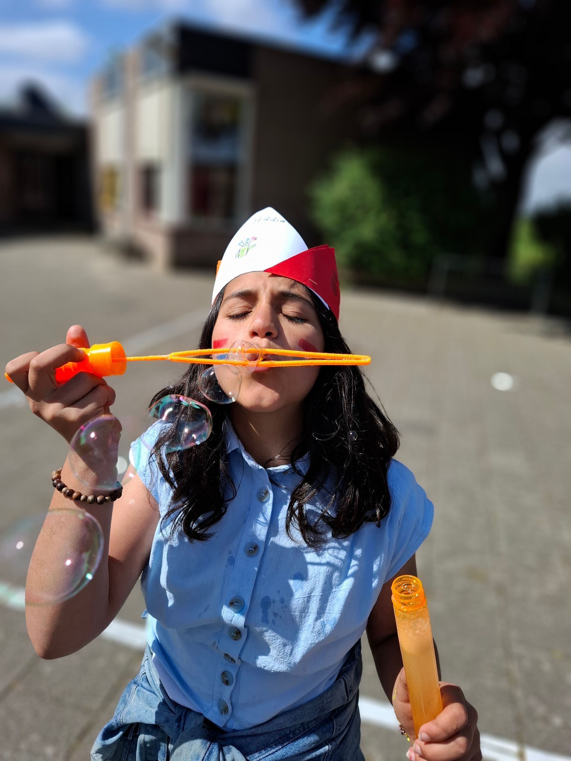 A girl wearing a red white and blue hat blowing soap bubbles