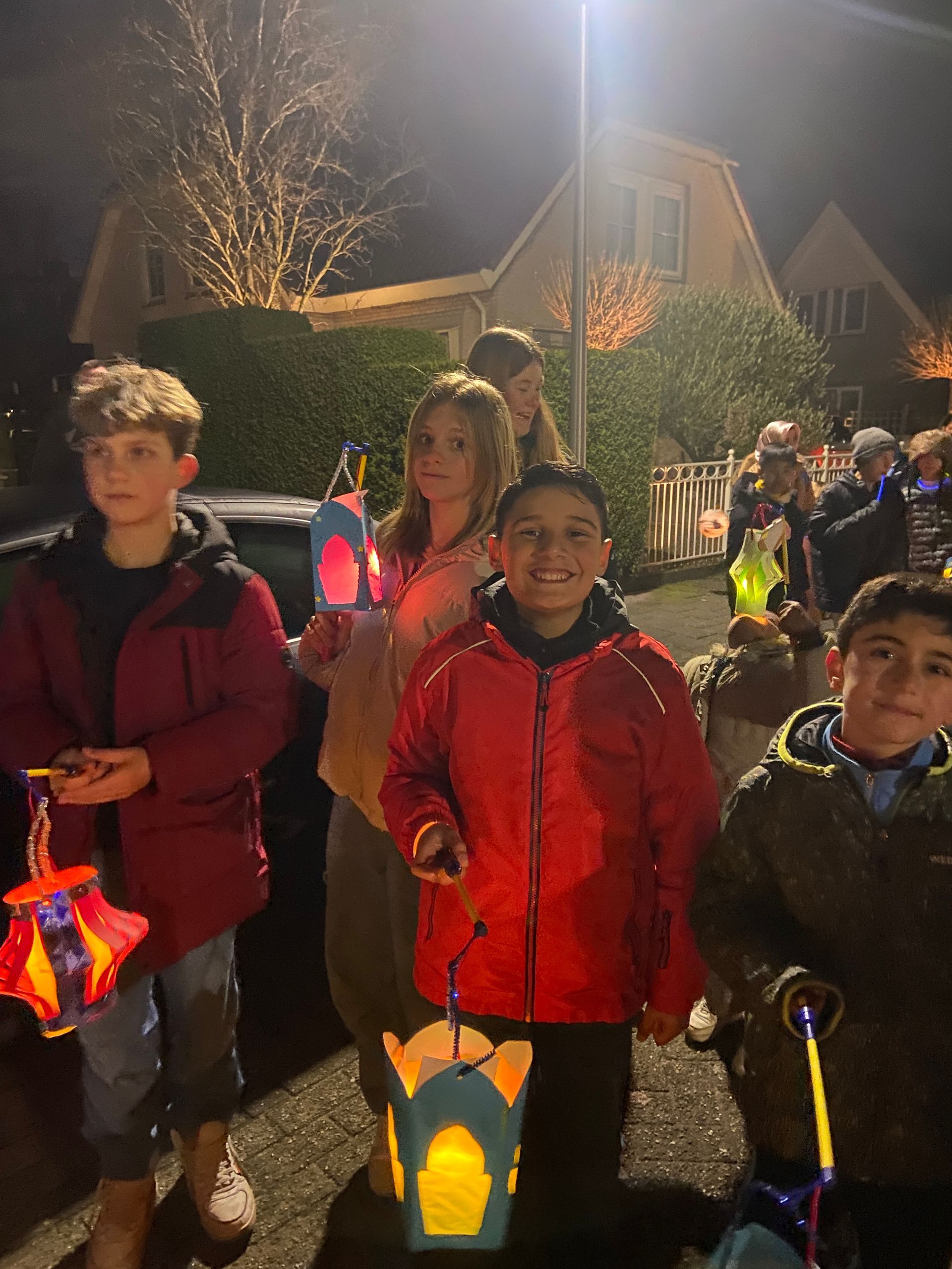 A group of children are holding lanterns in front of a car at night.
