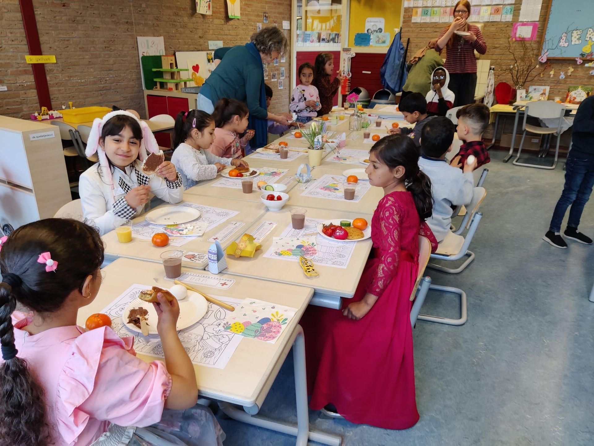 A group of children are sitting at tables in a classroom eating food.