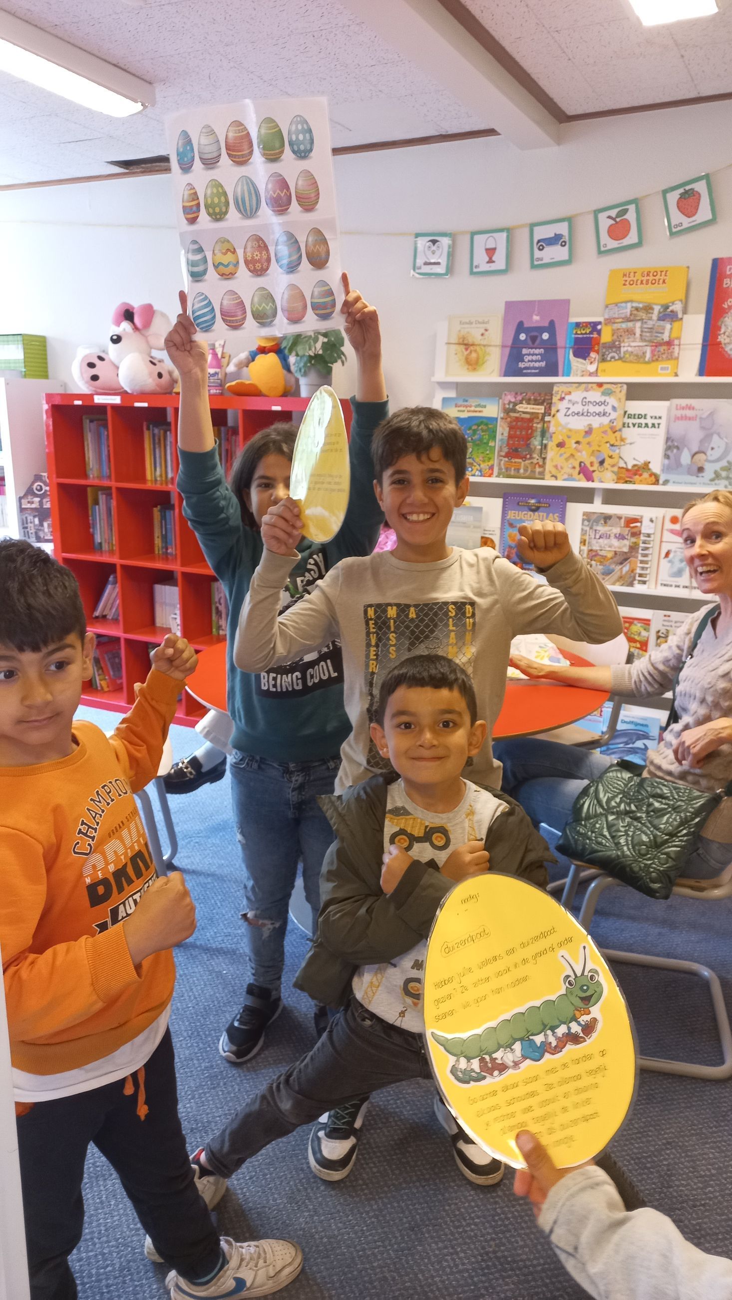 A group of children are holding up easter eggs in a library.