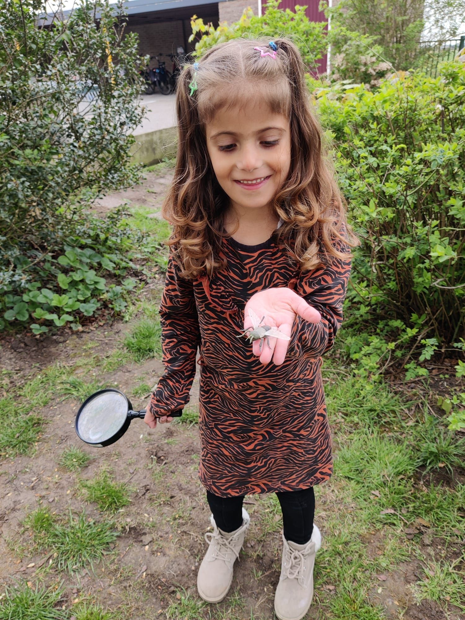 A little girl is holding a magnifying glass and a rock in her hand.
