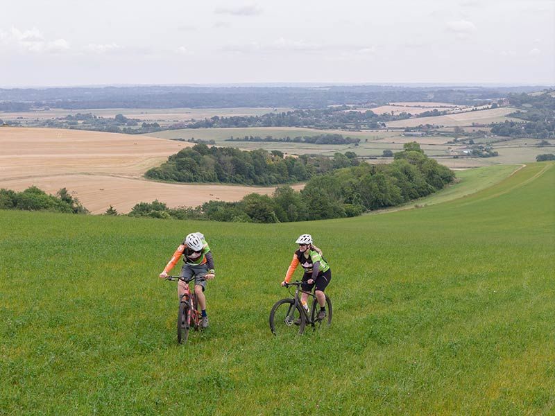 A man and woman striding across the green grass of The South Downs National Park.