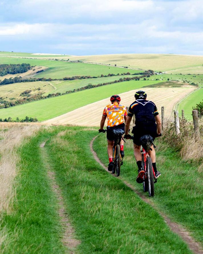 Two cyclists on one of the many bridle, cycle and footpaths on the South Downs, surrounded by rolling hills and  fields.