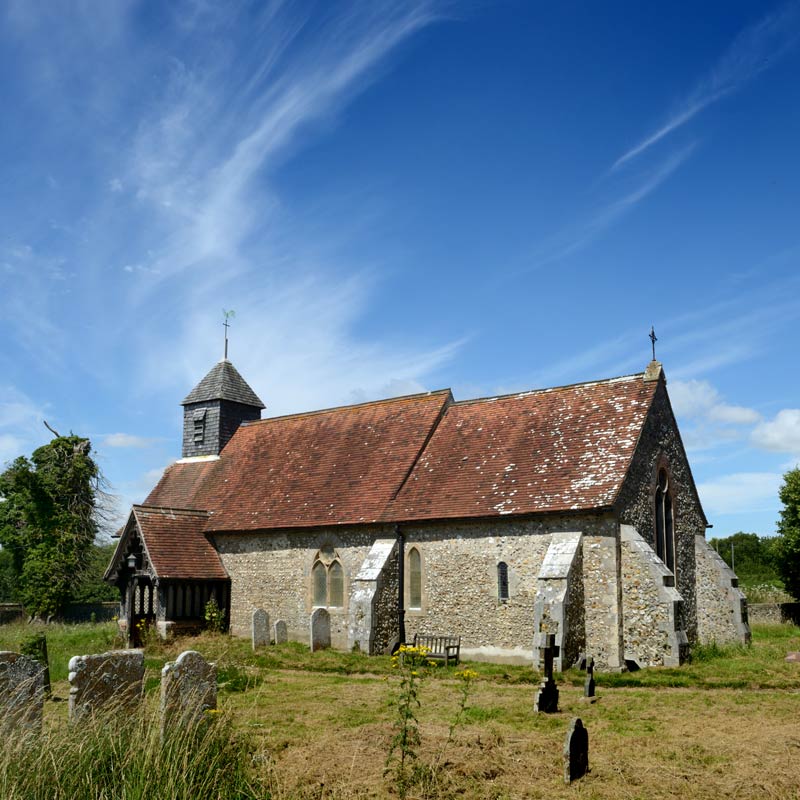 An historic  Sussex village church with churchyard, wildflowers and trees in the height of summer.