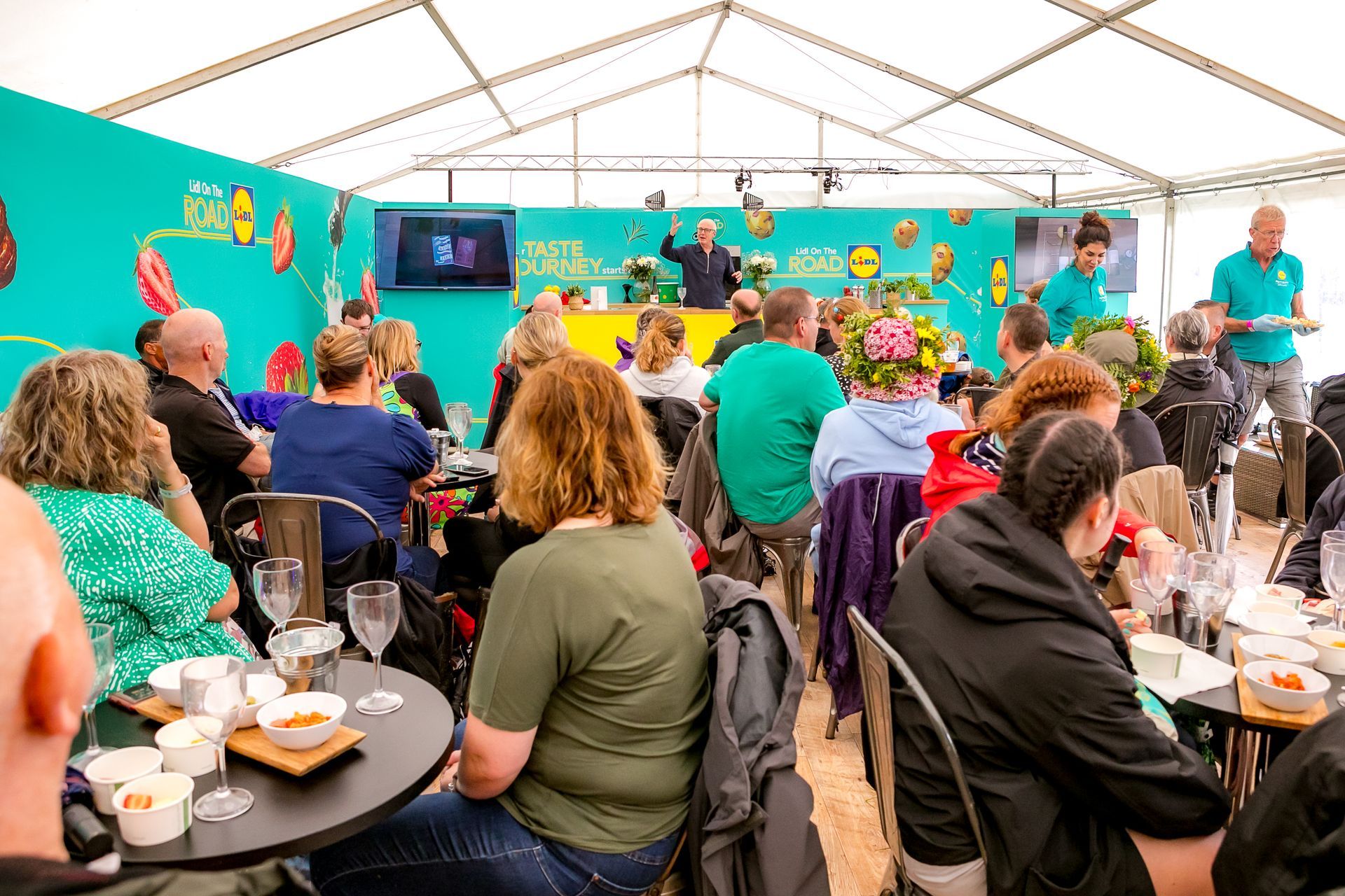 Woman with glasses gestures while speaking at a table, people listen.