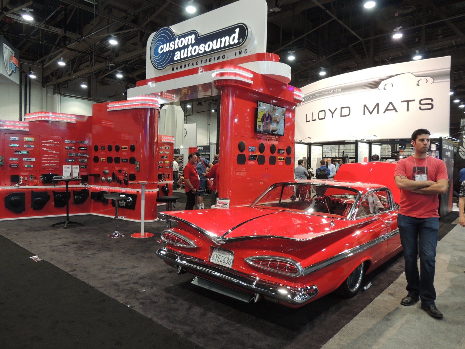 A man is standing in front of a red car at a car show.
