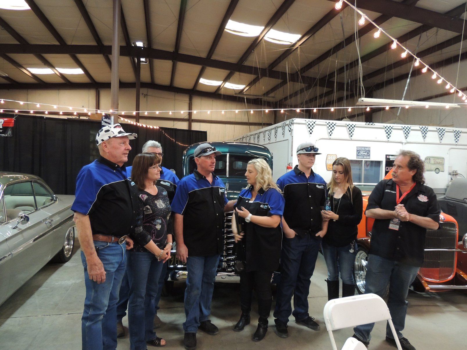 A group of people standing in front of a car in a garage.