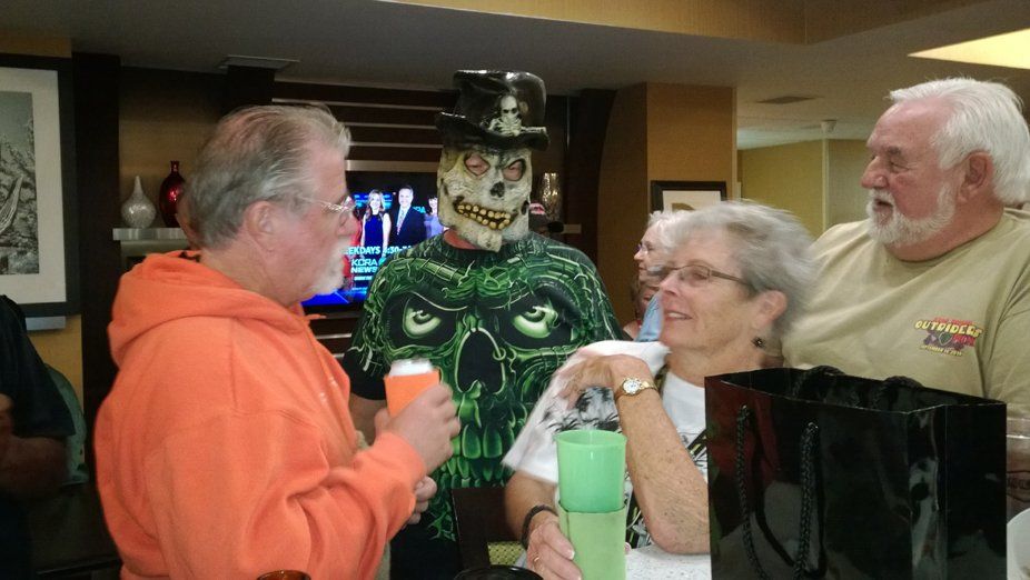 A group of people are standing around a man in a skull mask.