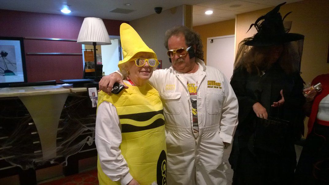 A man in a yellow crayon costume is standing next to a woman in a witch costume.