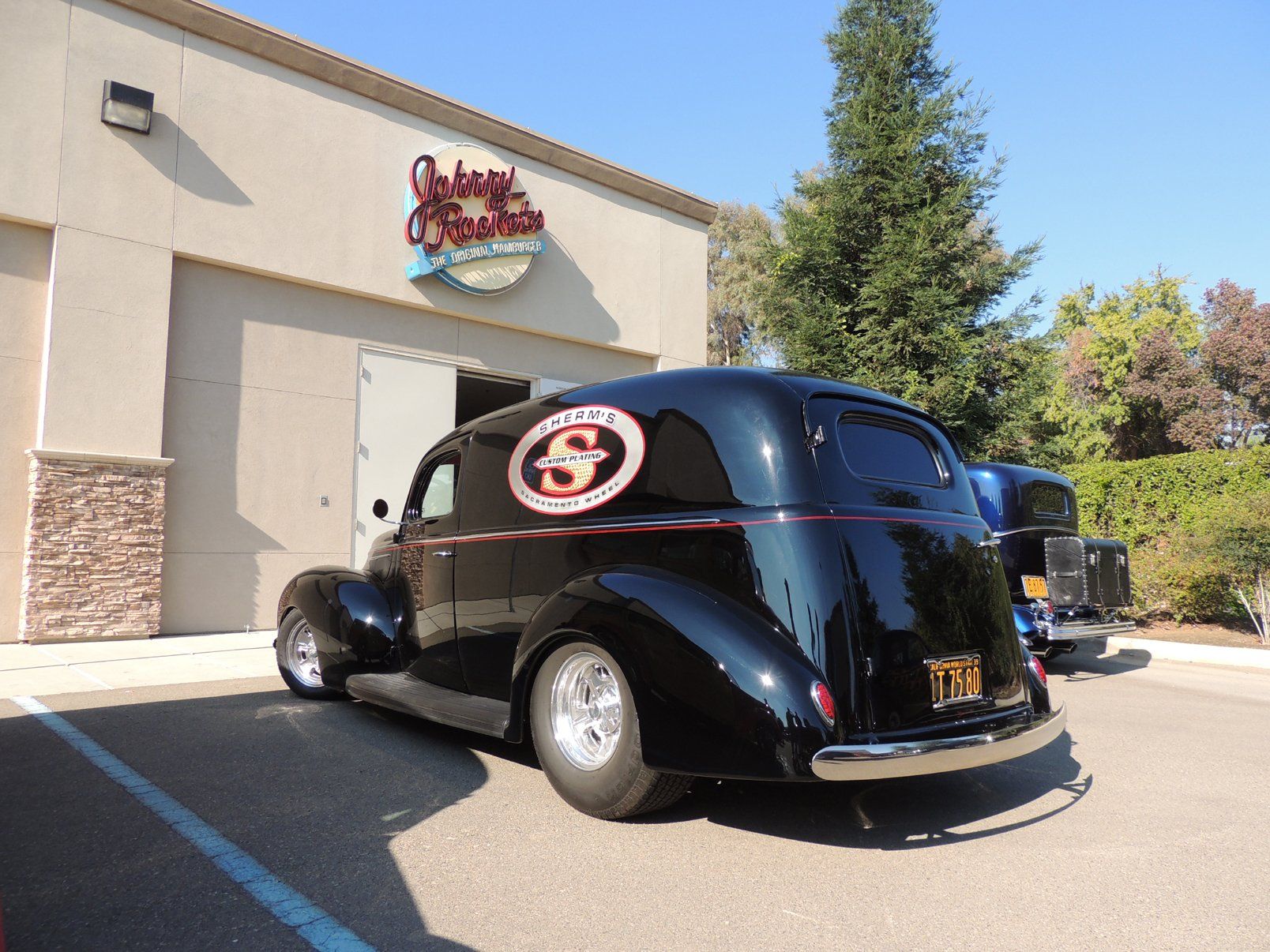 A black car with the letter s on the side is parked in front of a building