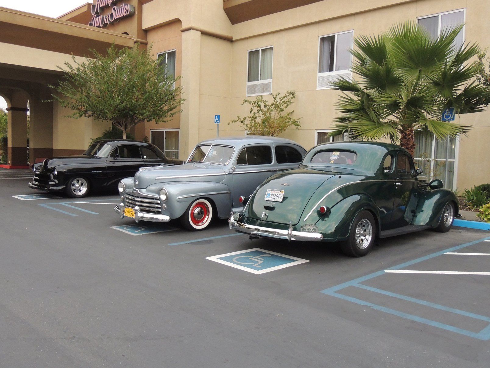 Three old cars are parked in front of a hotel