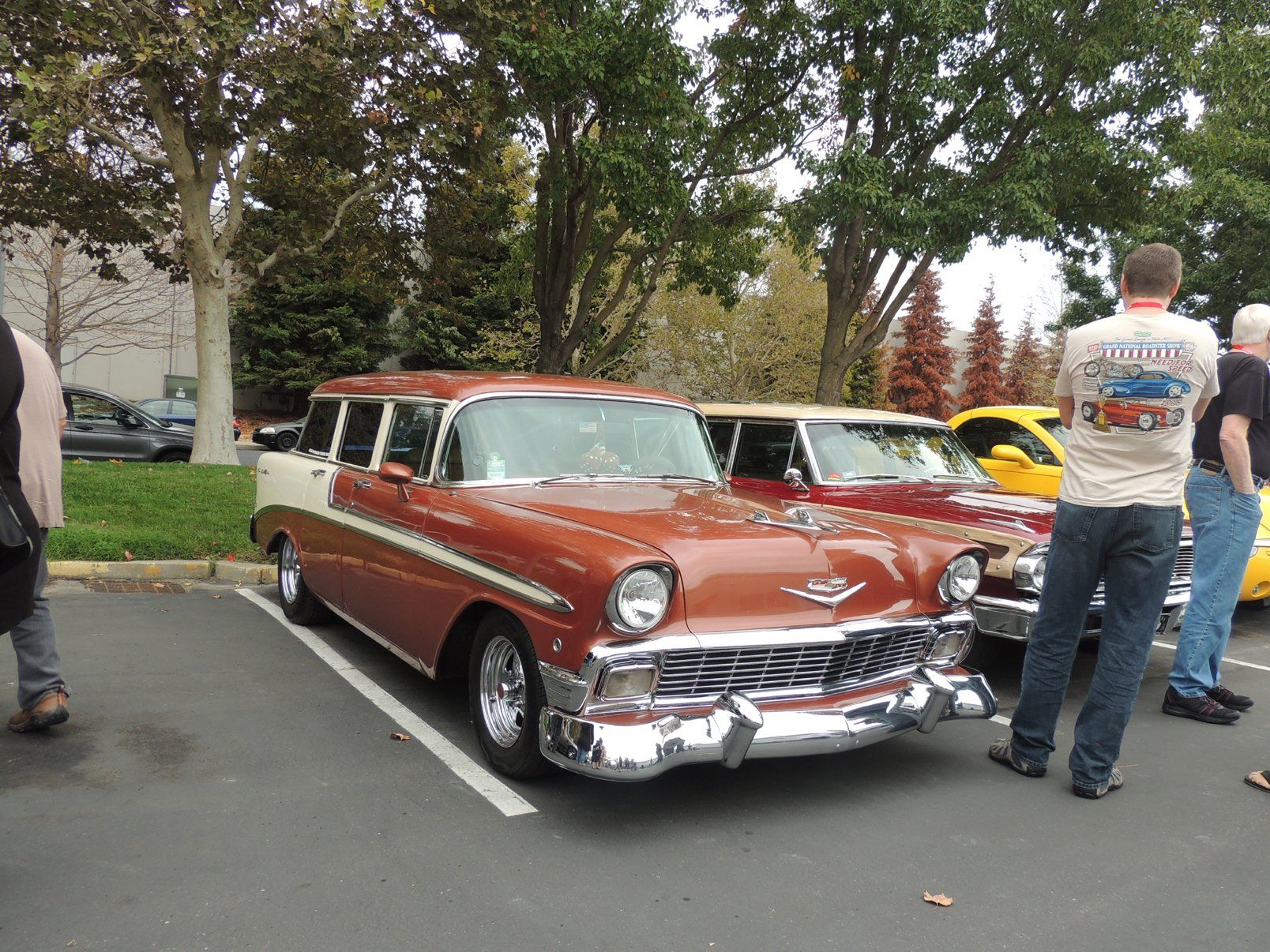 A man wearing a shirt that says california is standing next to a red car