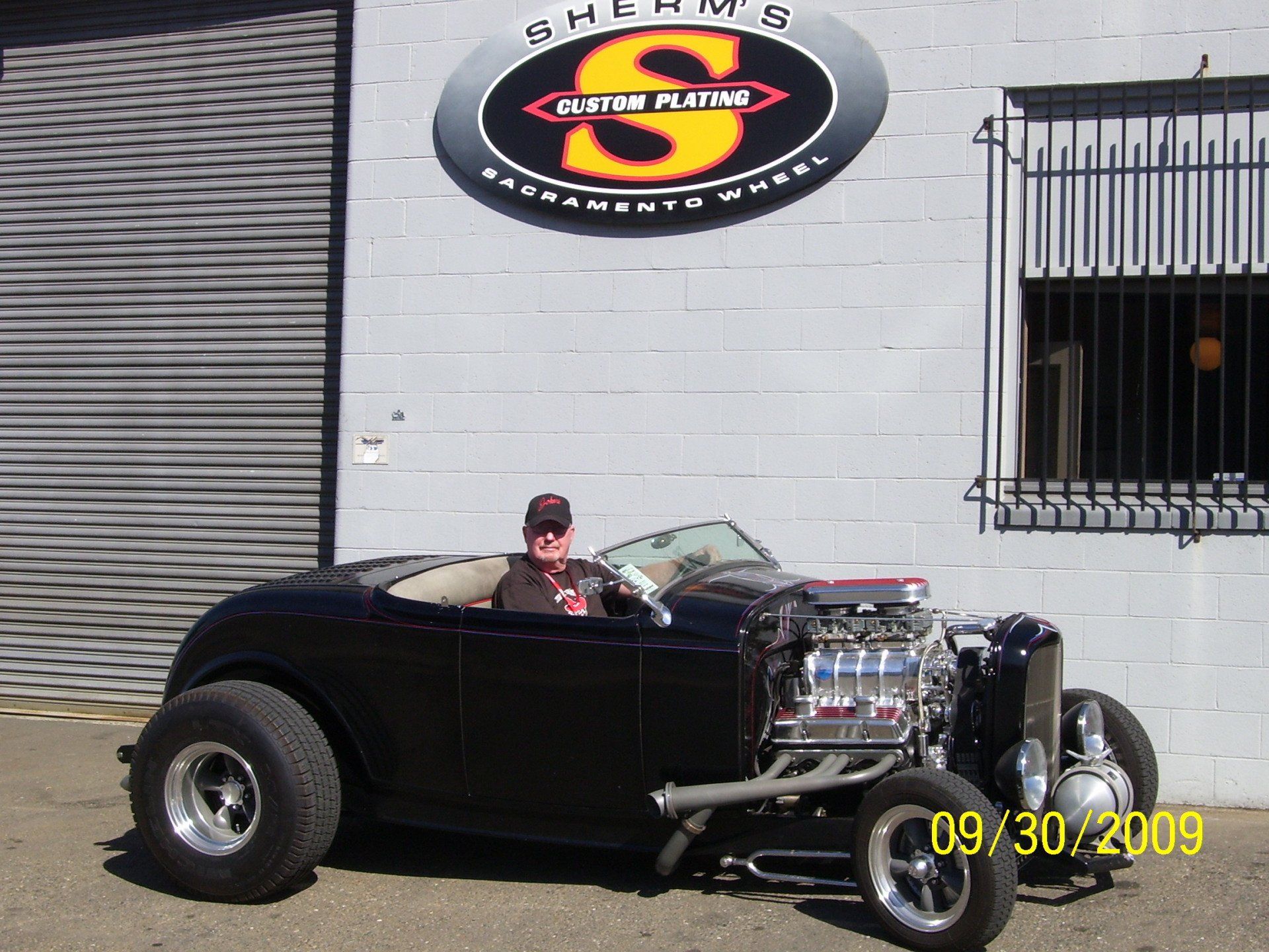 A man is sitting in a black car in front of a building with the letter s on it