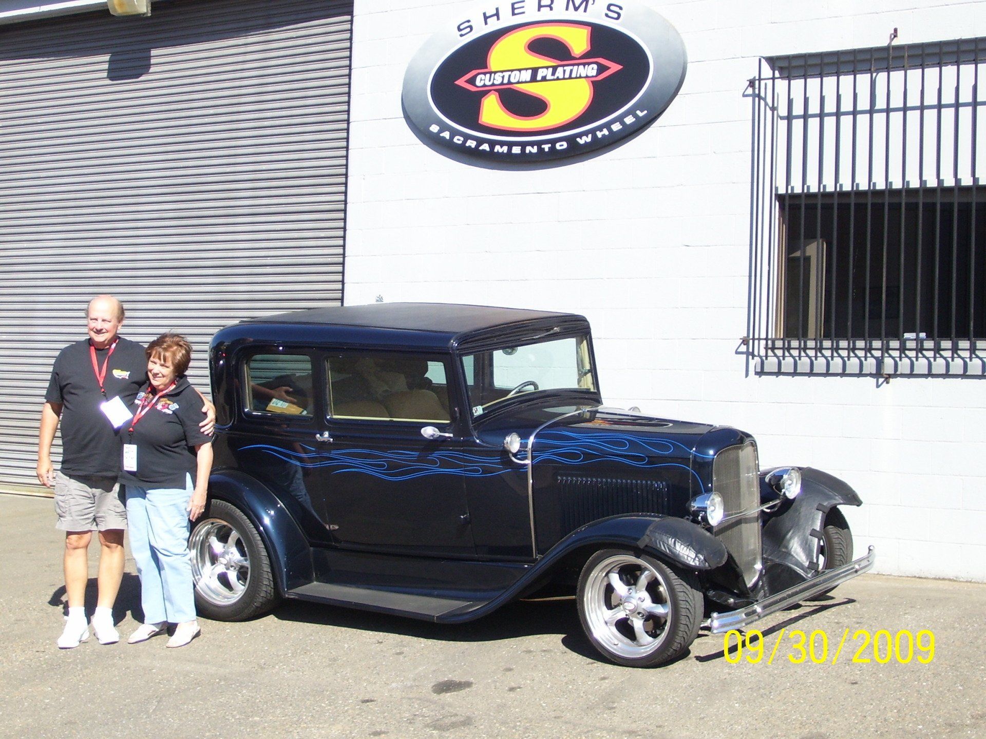 A couple standing next to a car in front of a building with the letter s on it