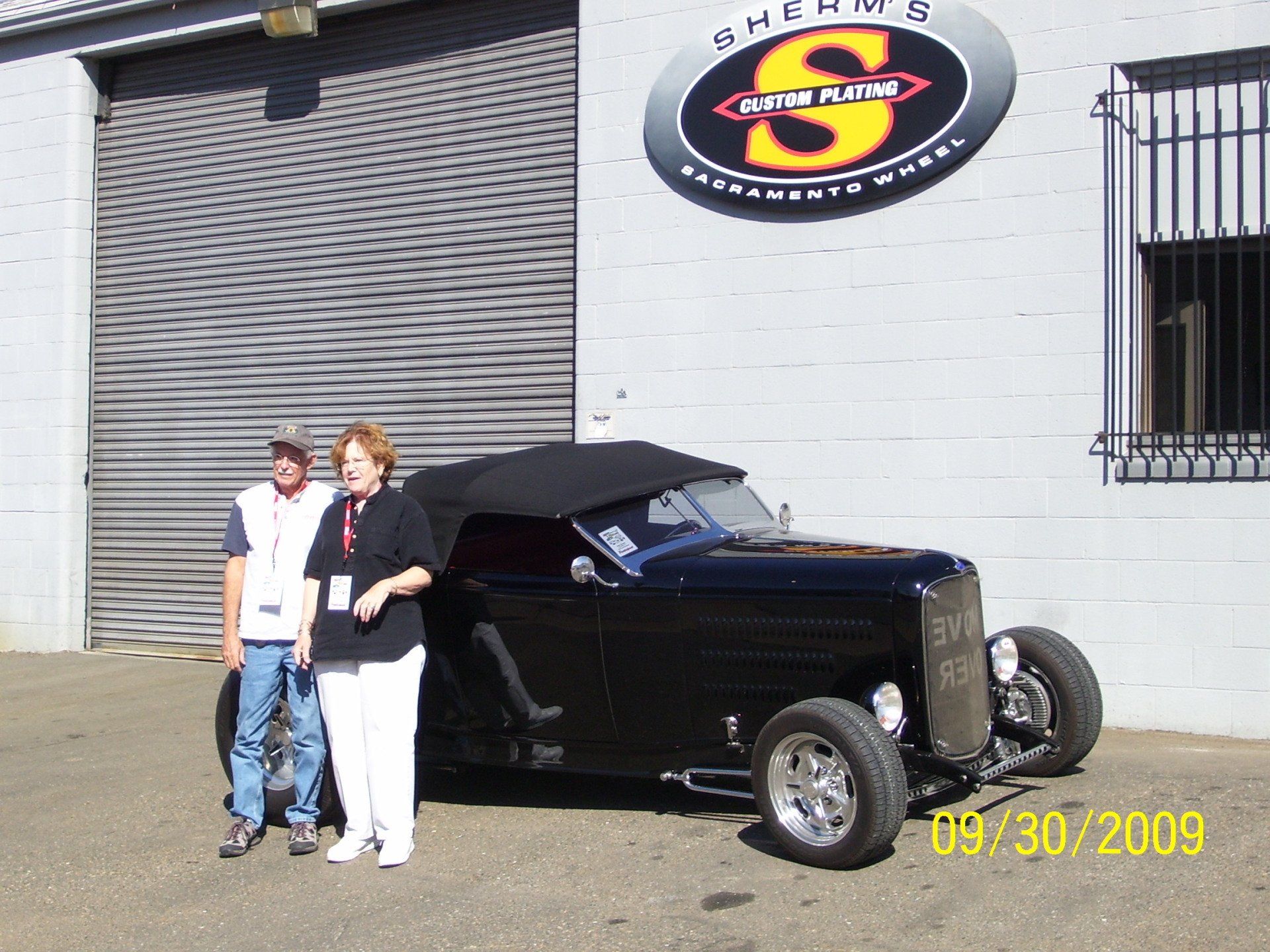 A couple standing next to a black car in front of a building with the letter s on it