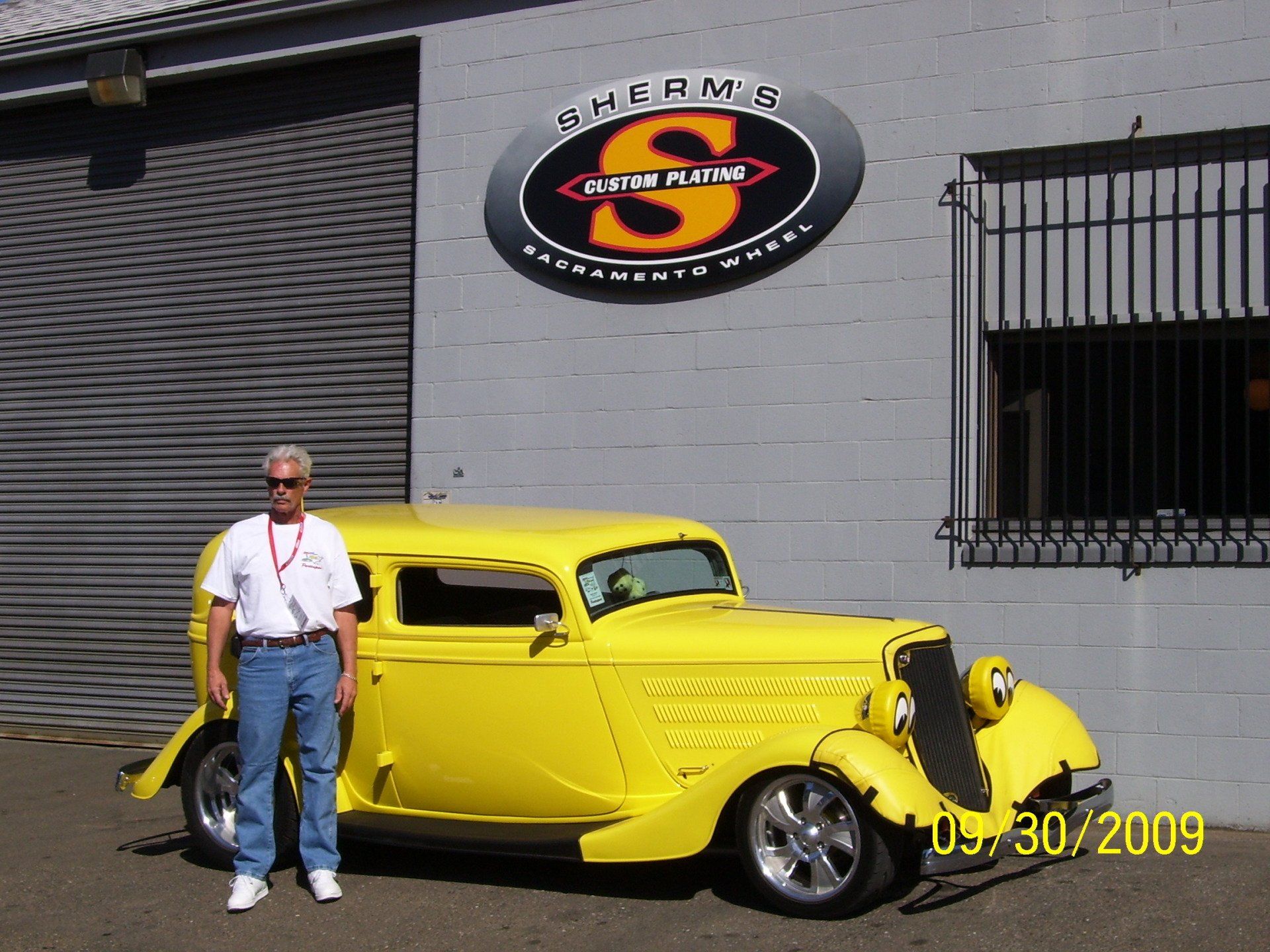 A man is standing next to a yellow car in front of a building with the letter s on it