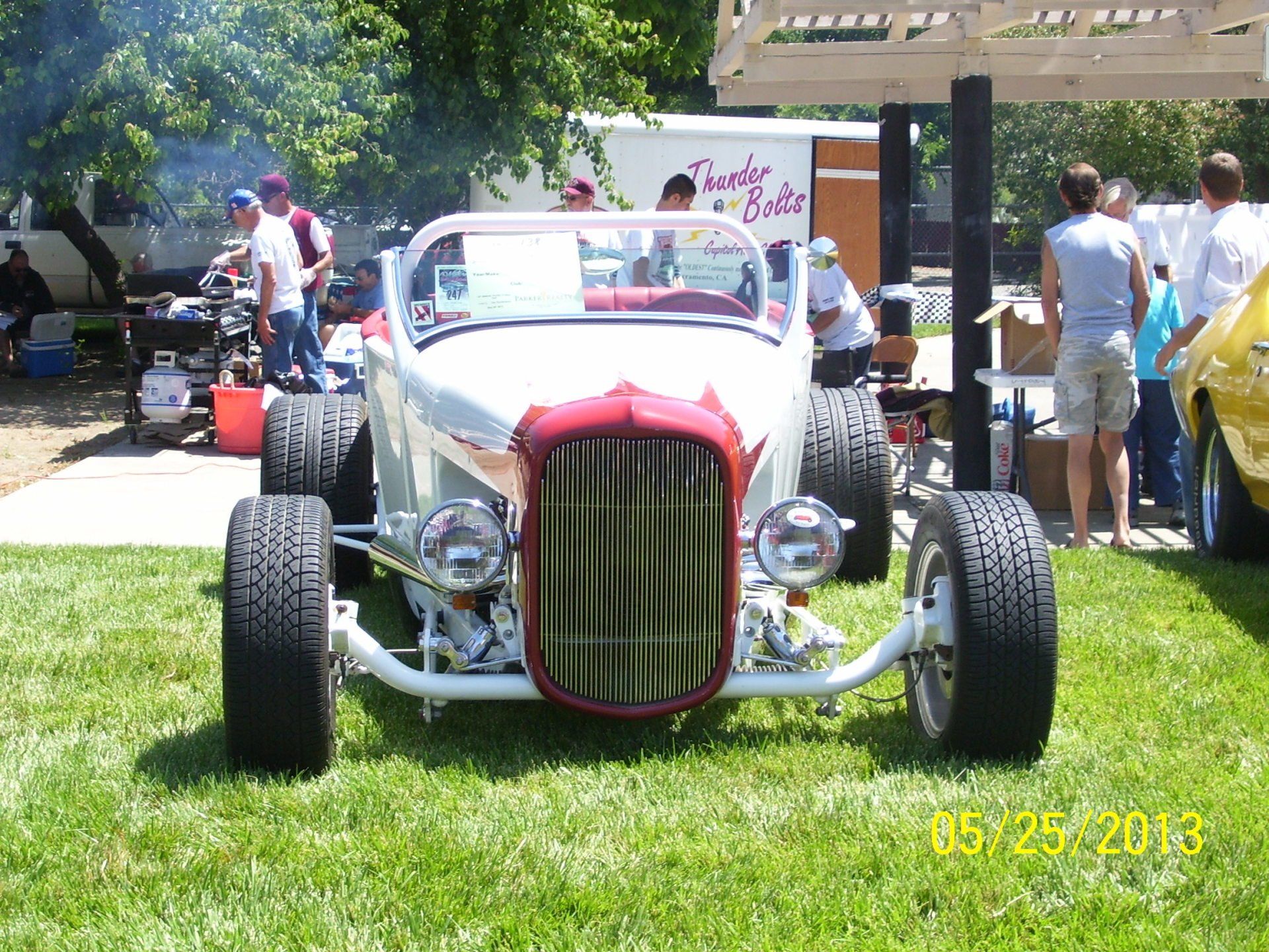 A white car with a red hood is parked in the grass