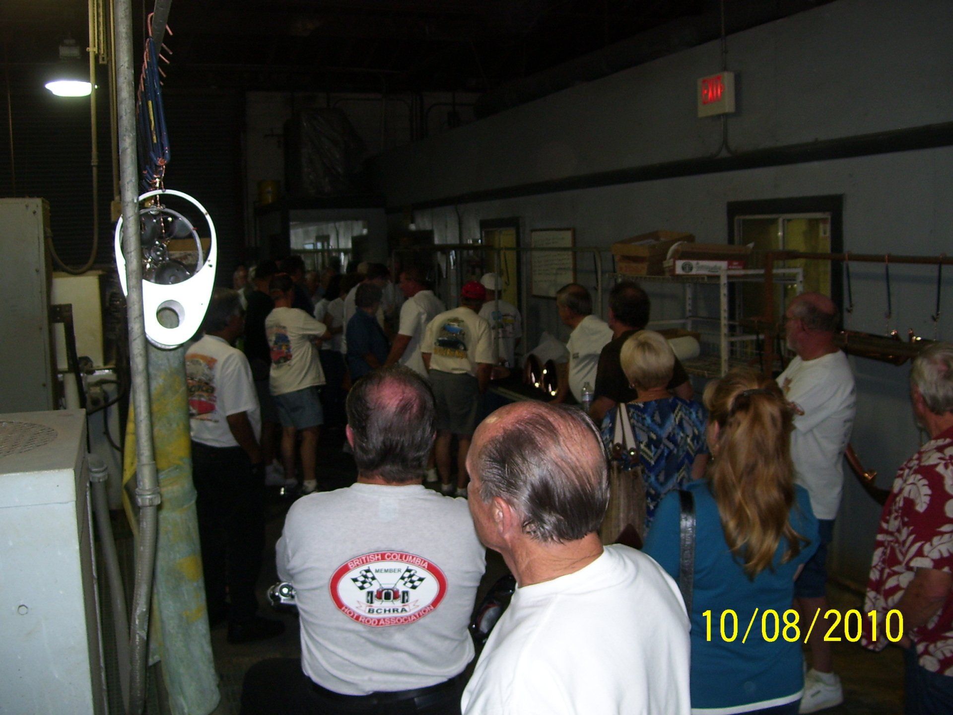 A group of people are gathered in a dark room and one man is wearing a shirt that says ' racing ' on it