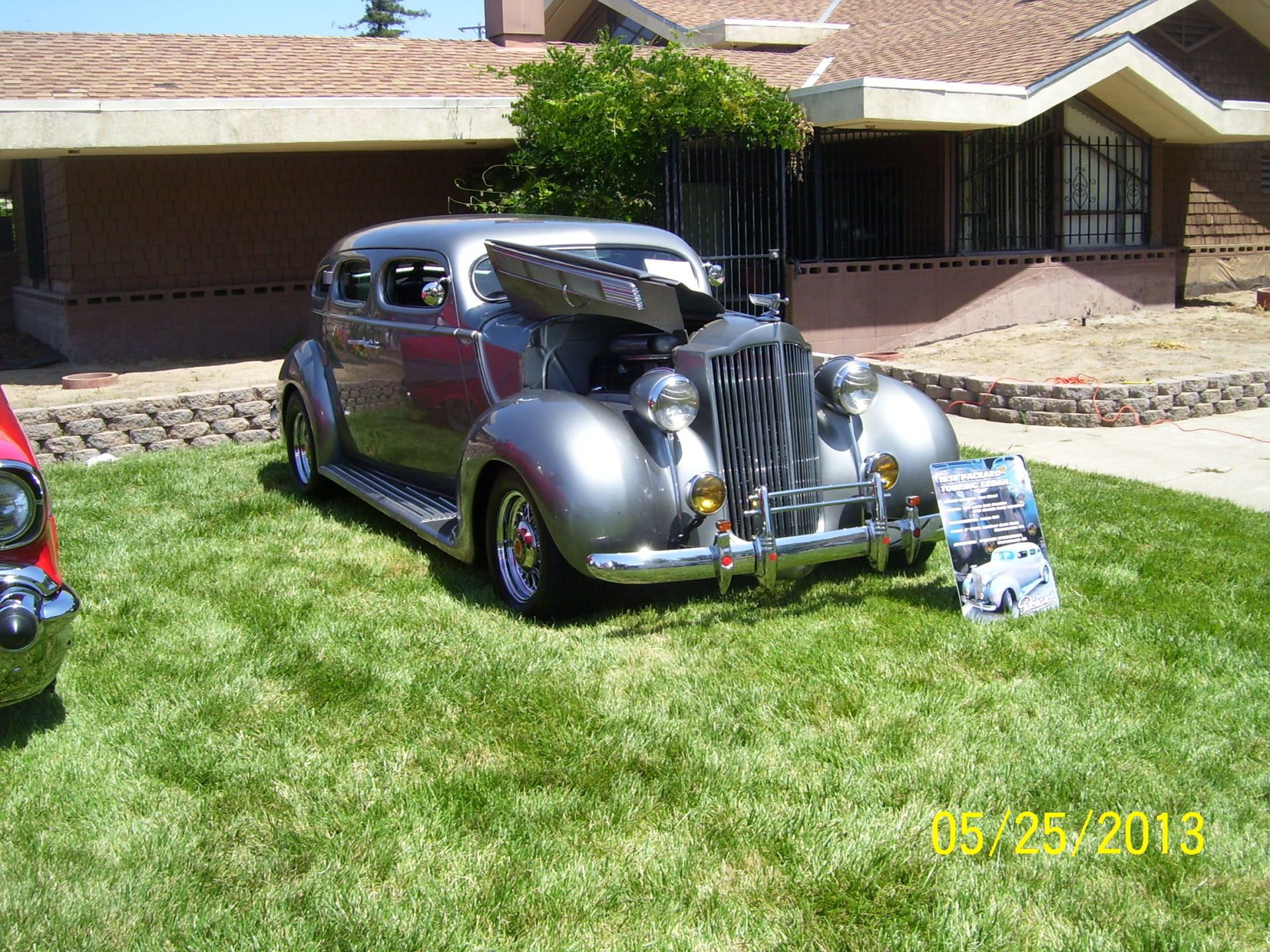 A silver car with the hood up is parked in front of a house