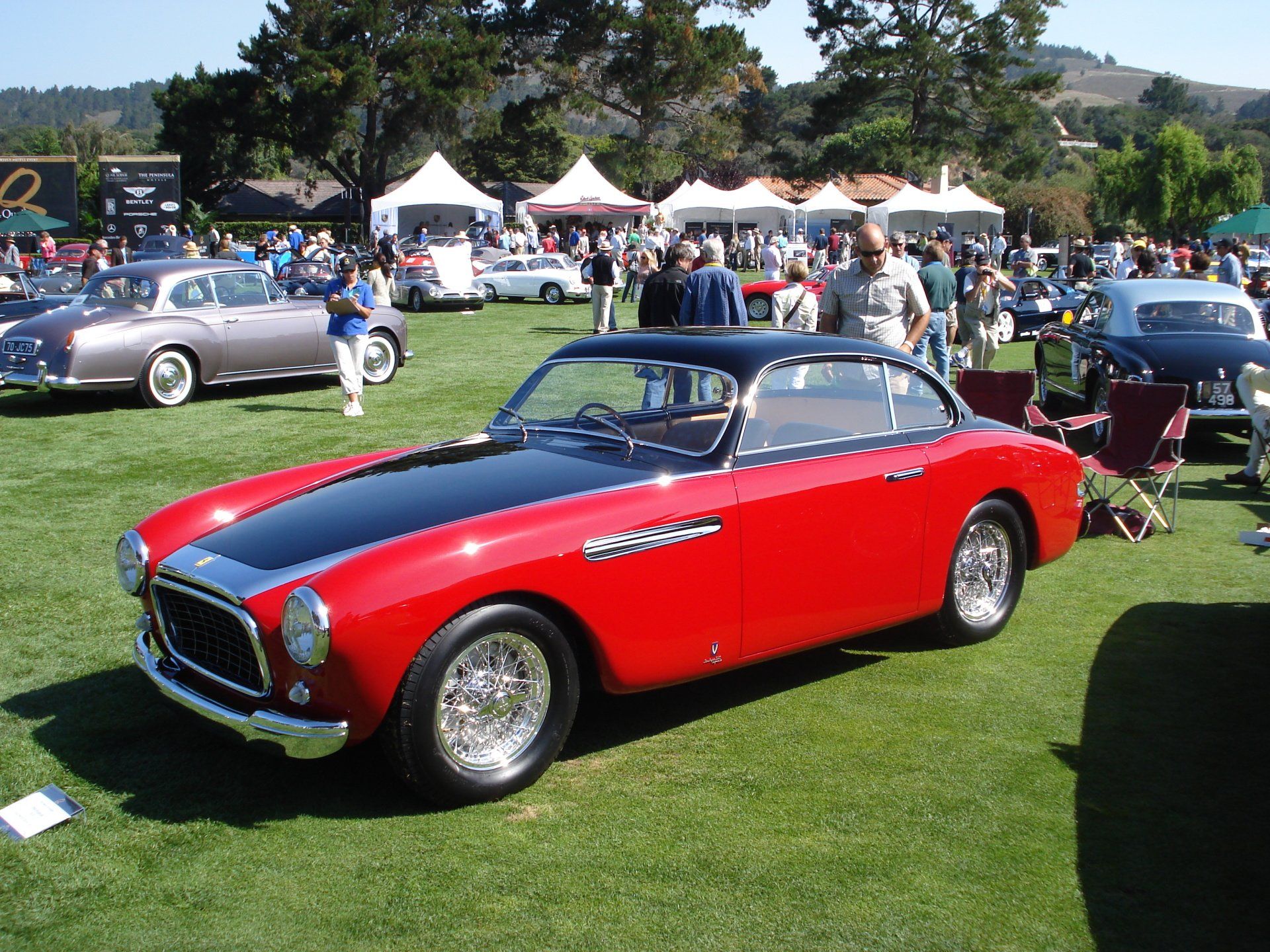 A red car with a black hood is parked in a grassy field