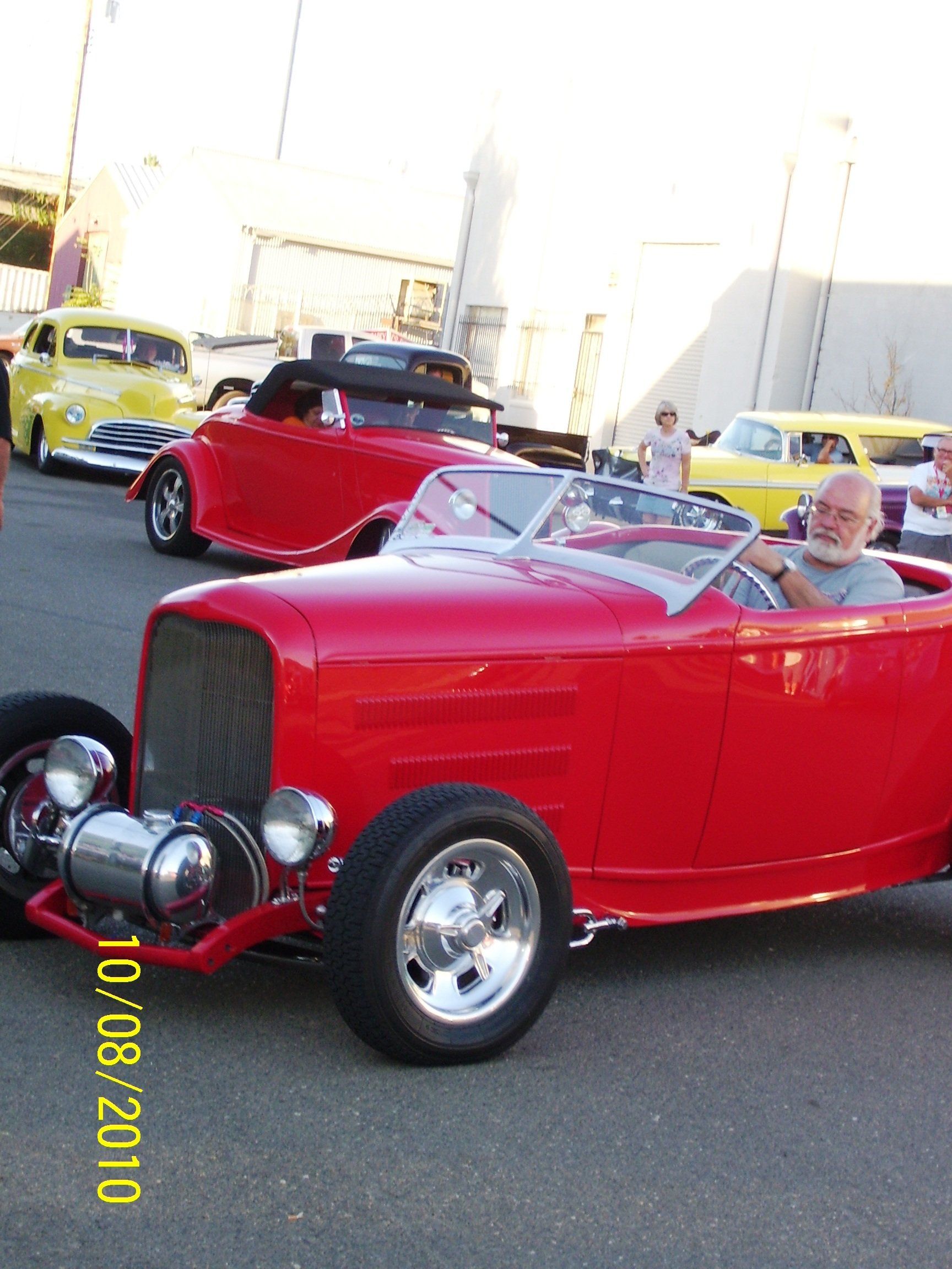 A man is sitting in a red car with the date 10/08/2010