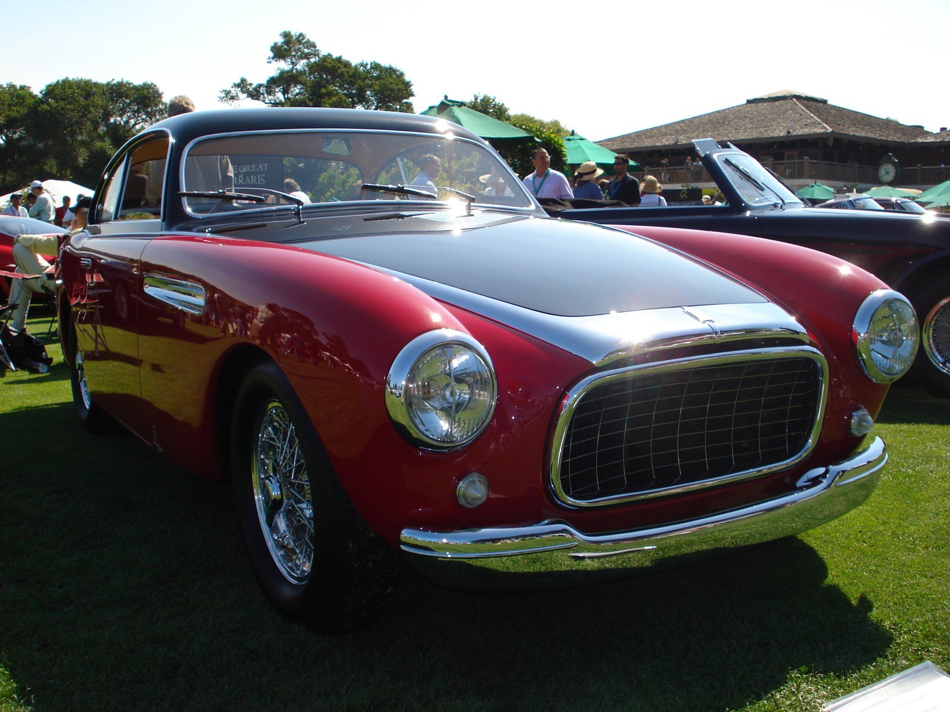 A red car with a black hood is parked on the grass