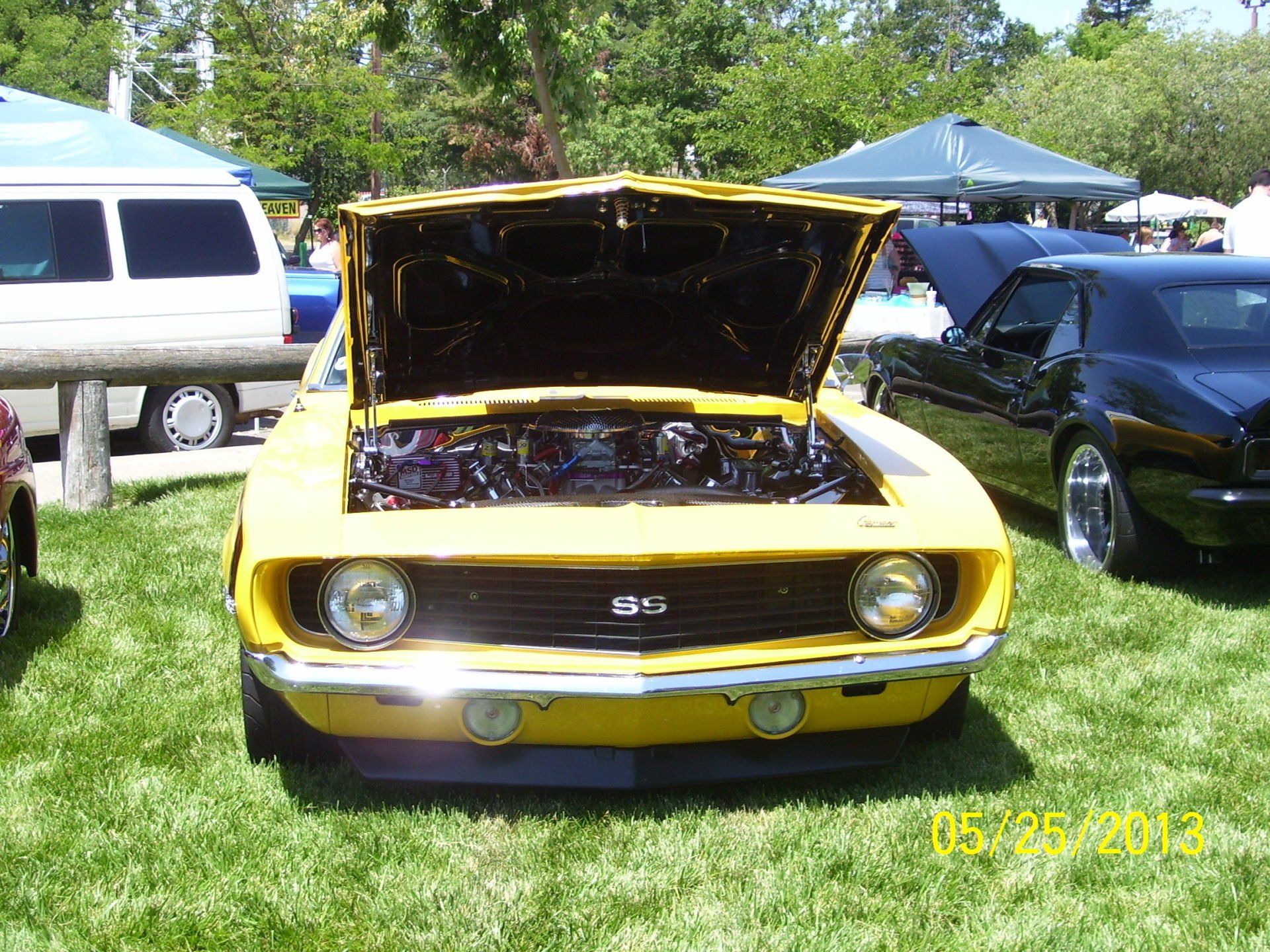 A yellow car with the hood up is parked in the grass