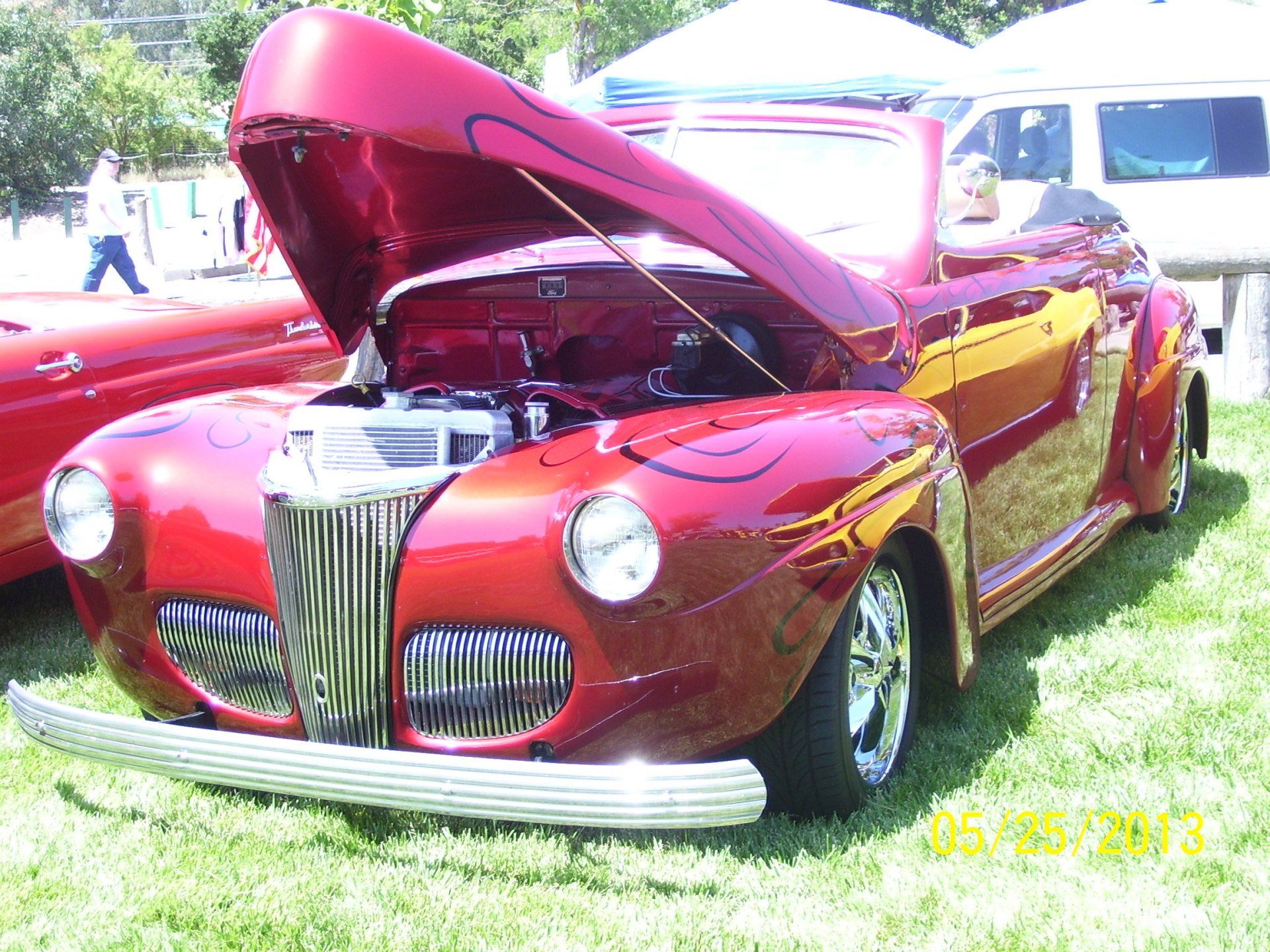 A red car with the hood up is parked in the grass