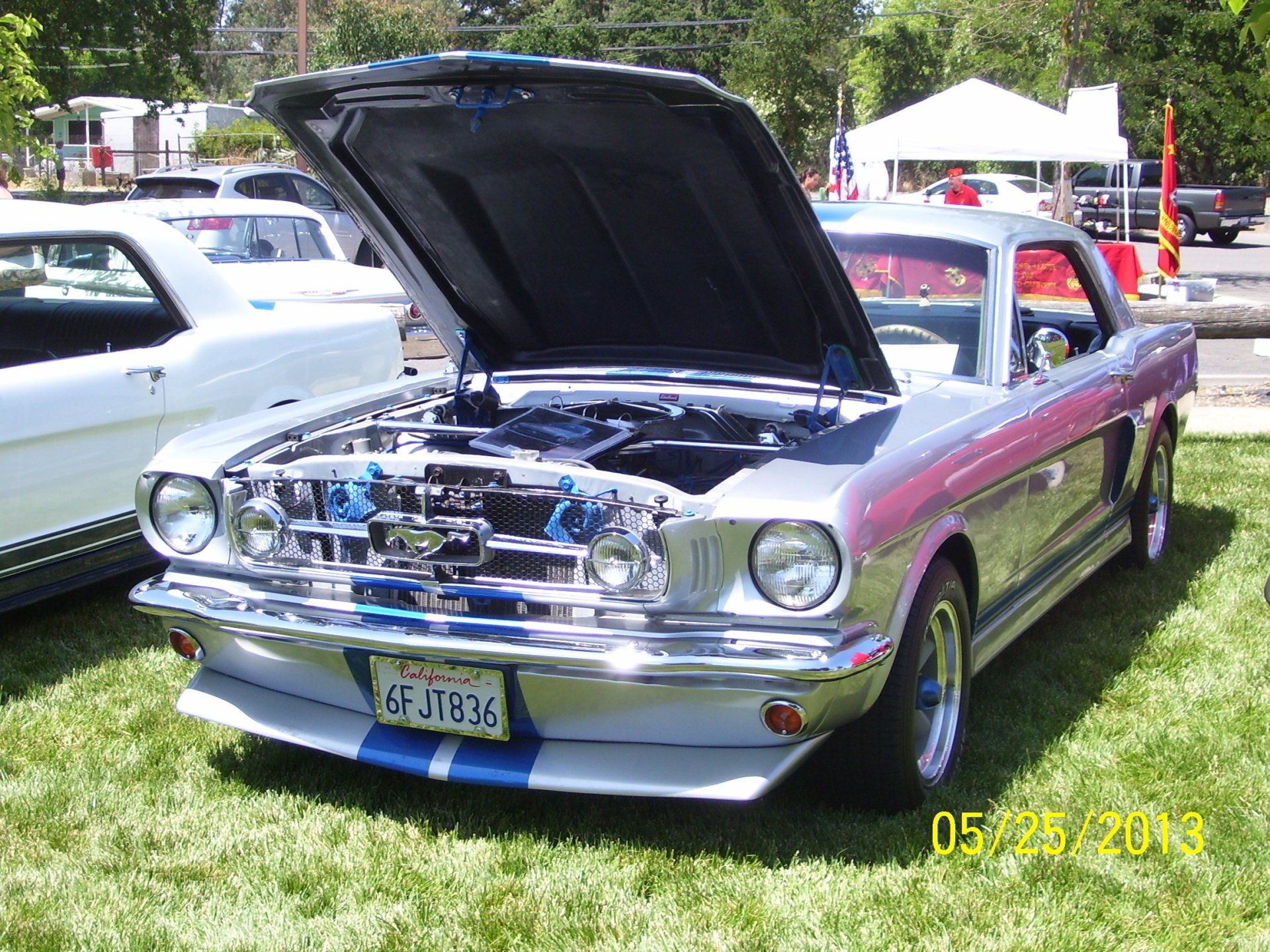 A silver mustang with the hood up is parked in the grass