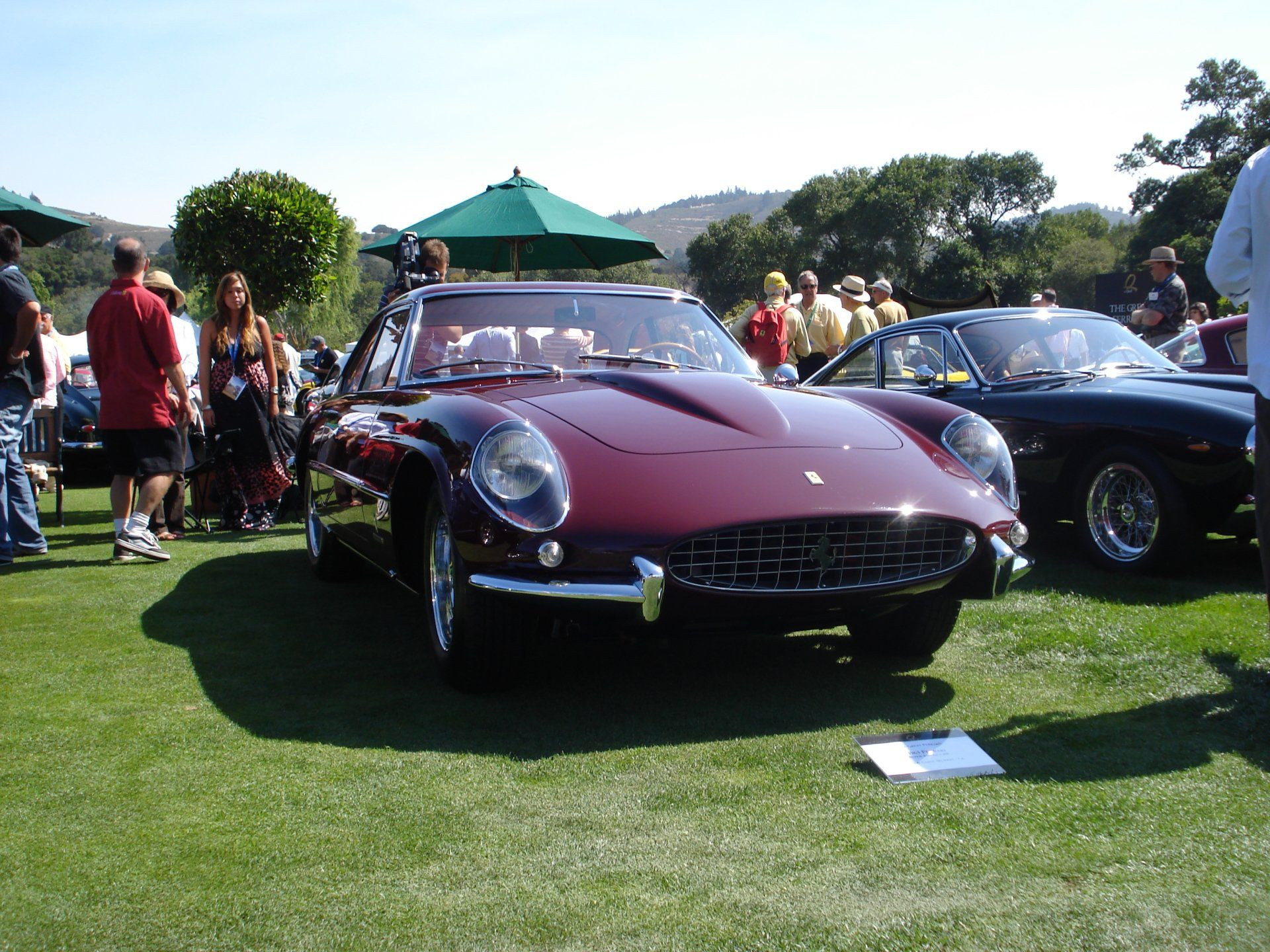 A burgundy car is parked in a grassy field at a car show