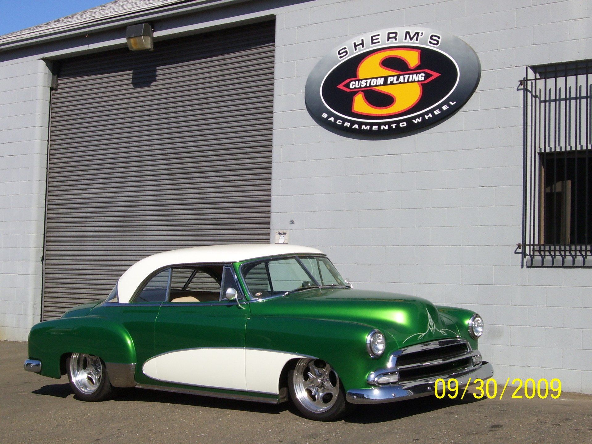 A green and white car is parked in front of a building with the letter s on it