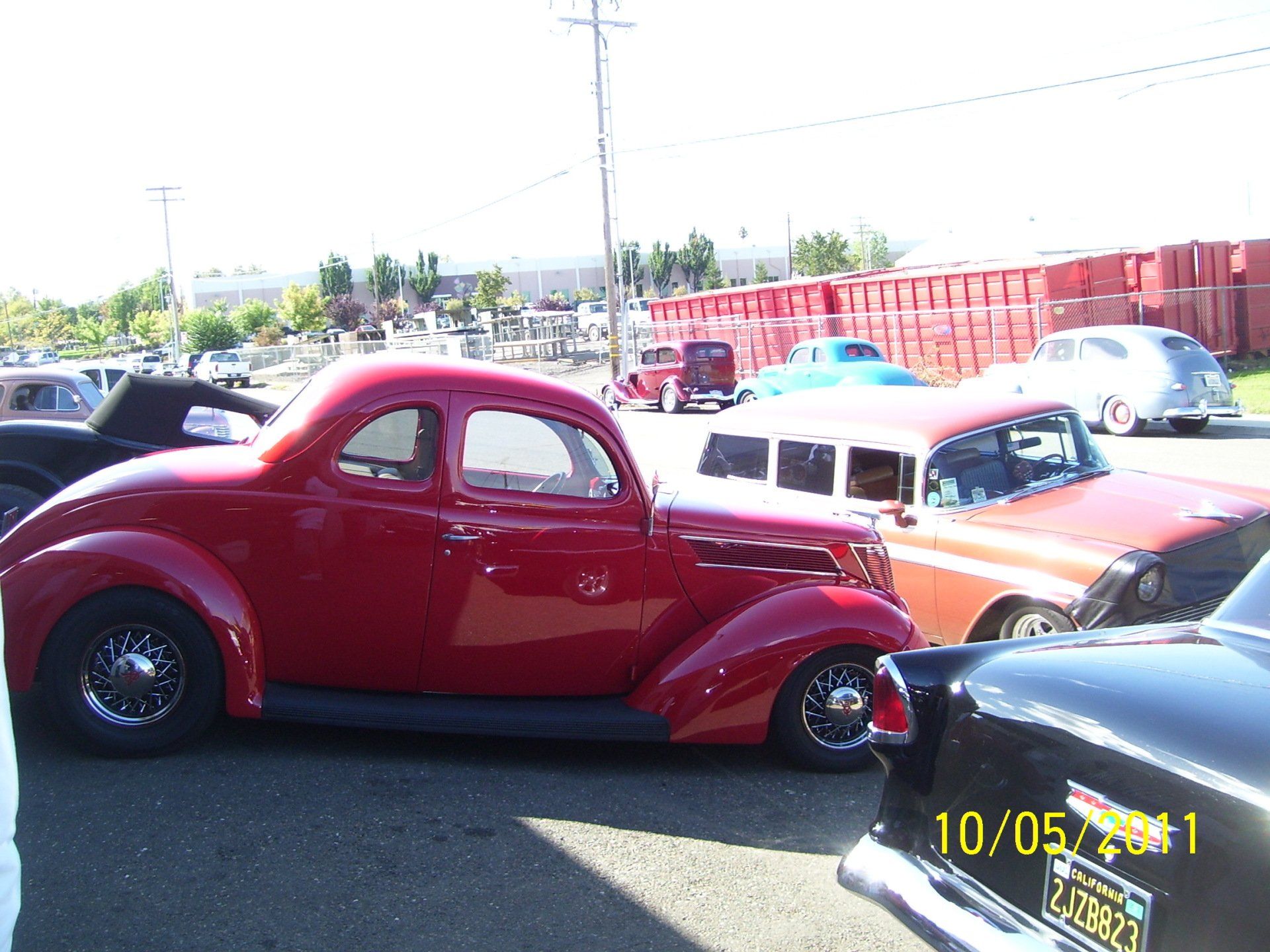A red car is parked in a parking lot with other cars