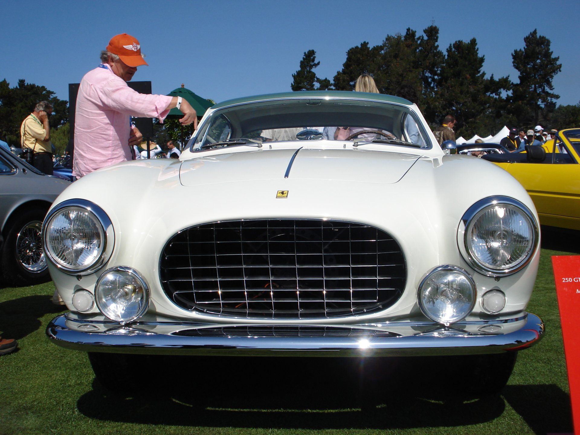 A man in an orange hat stands in front of a white car