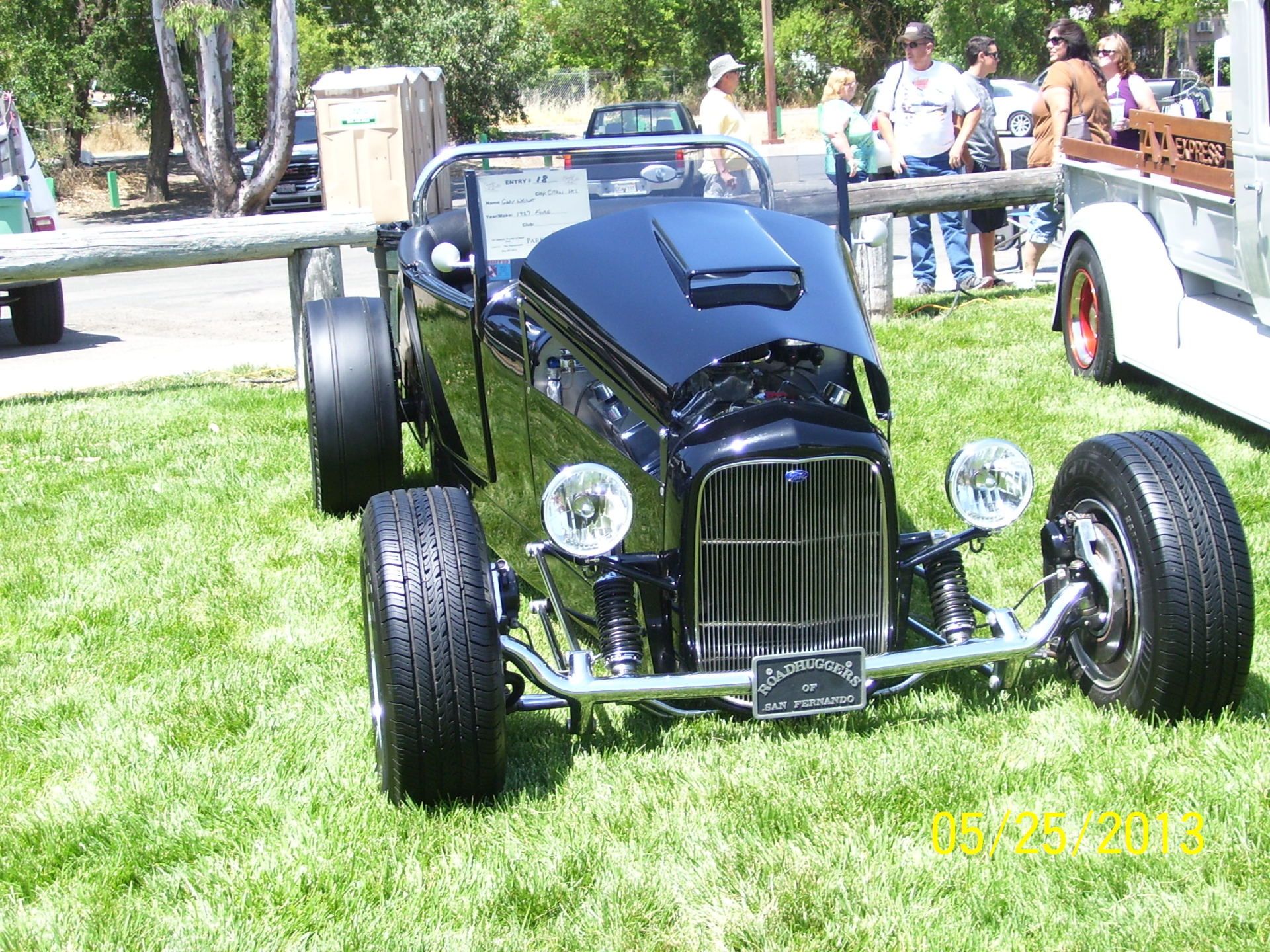 A black hot rod is parked in the grass at a car show