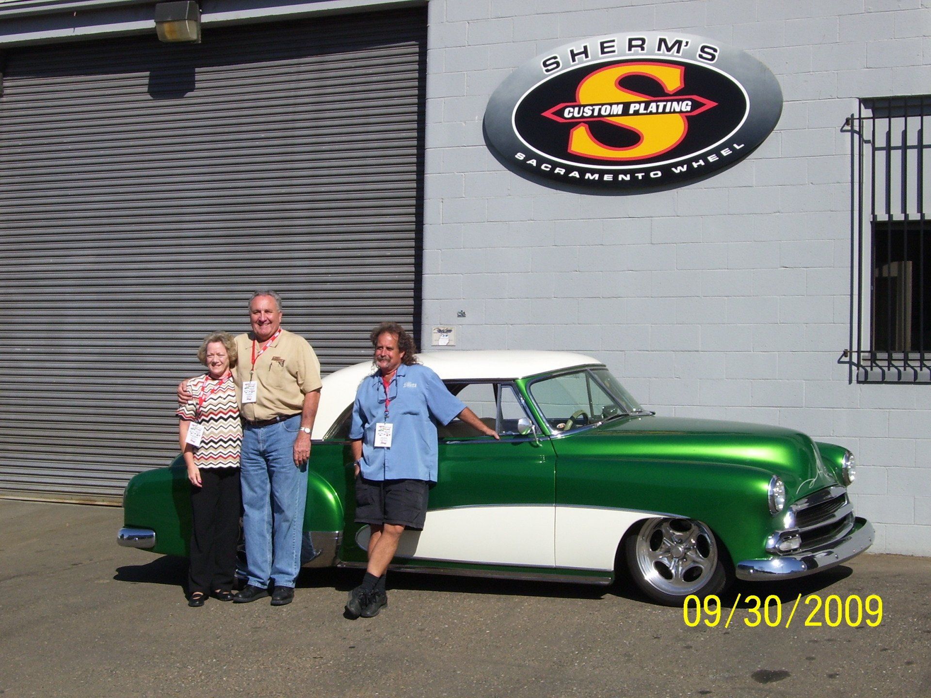 Three people standing in front of a green and white car