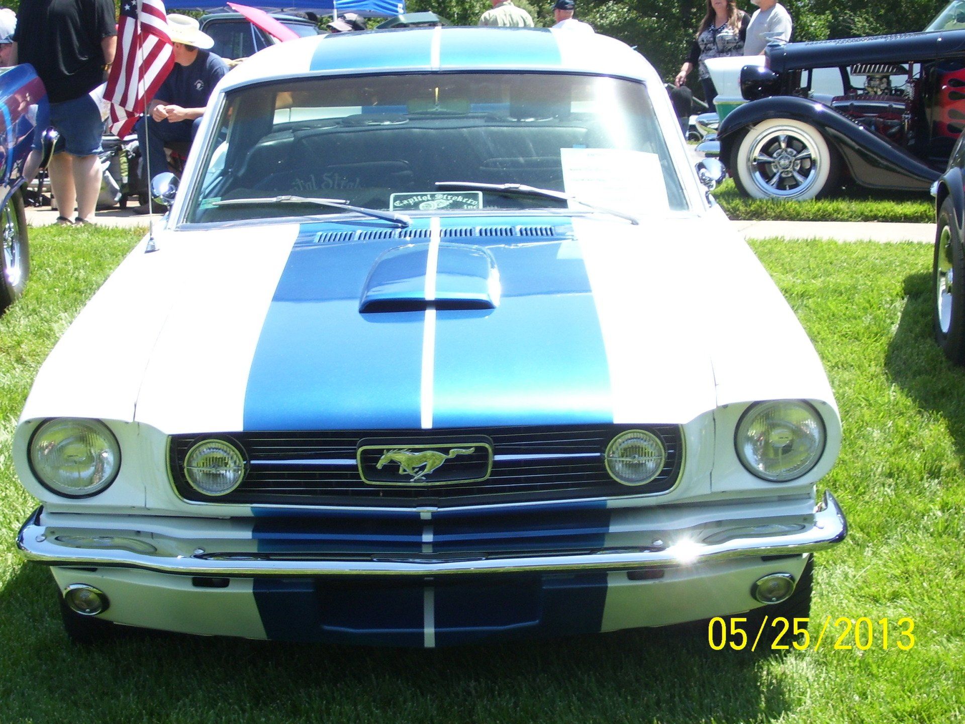 A blue and white mustang is parked in the grass