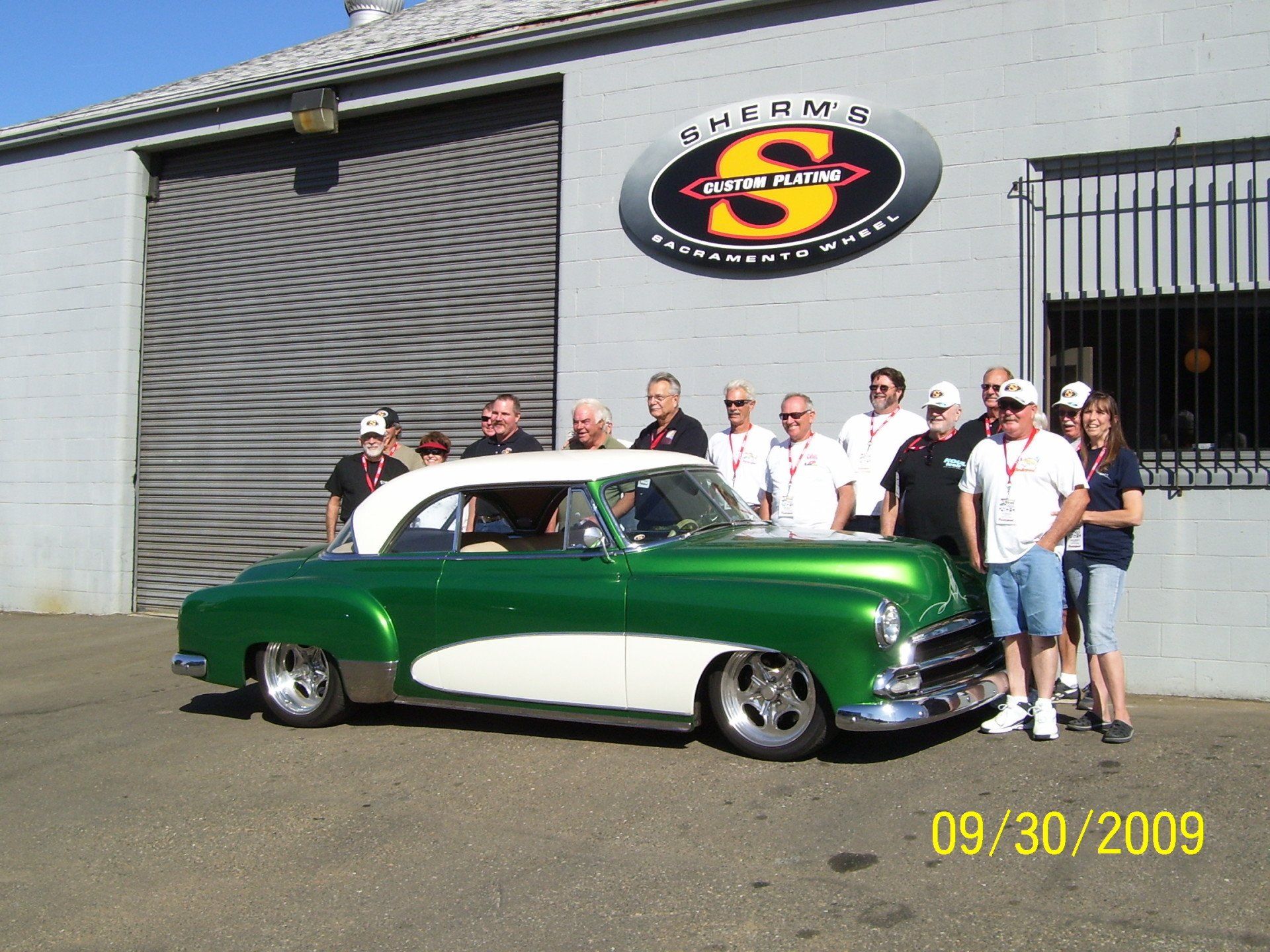A group of people standing in front of a green and white car